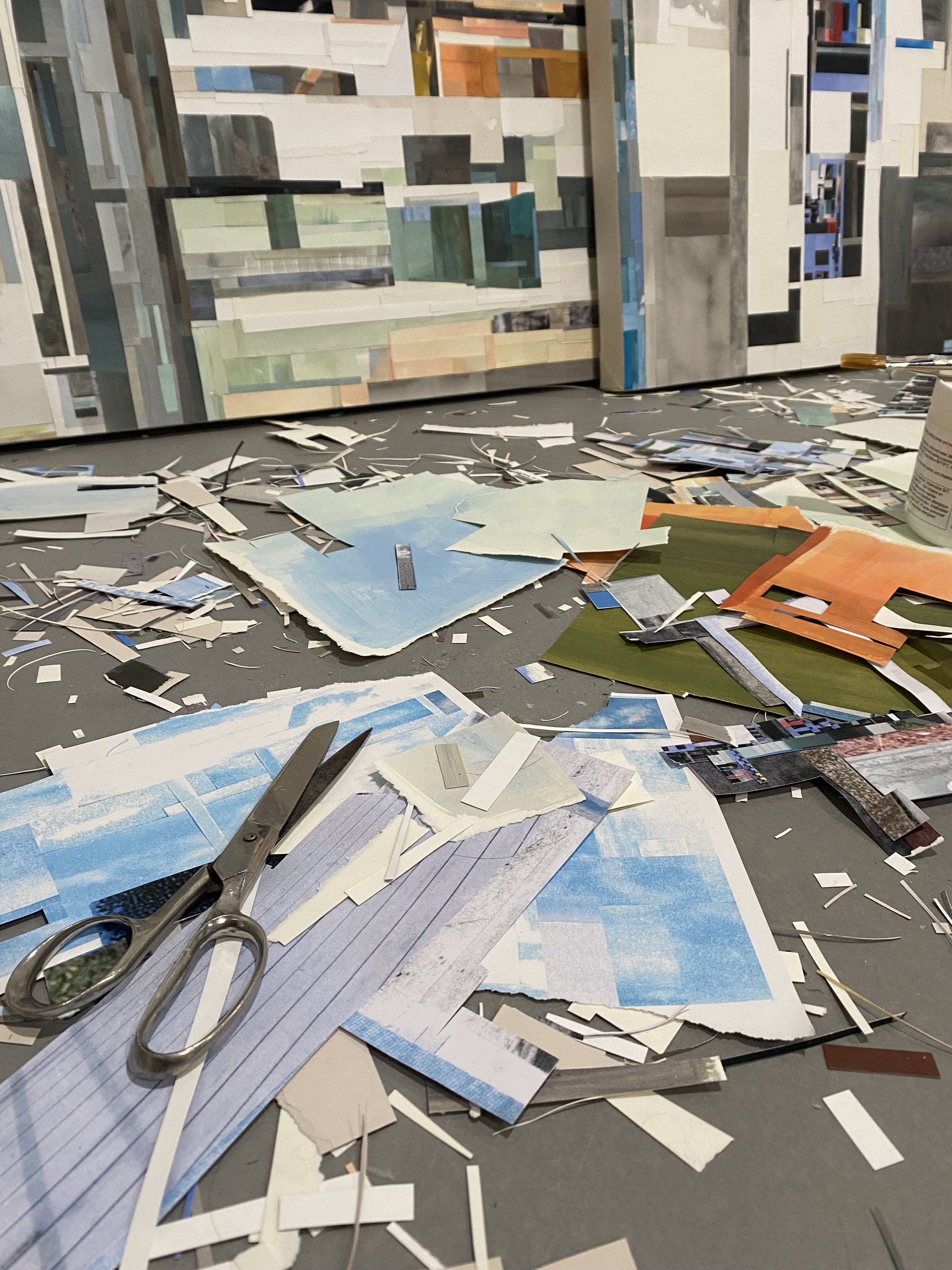 Image of artist's studio showing in process collage work and leftover paper, scissors.