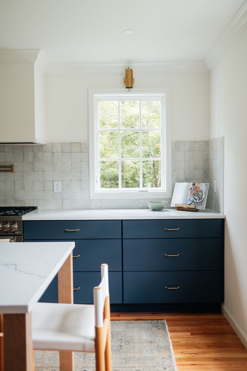 Modern kitchen with navy blue cabinets, white countertops, a large window, a beige tile backsplash, and hardwood floors.