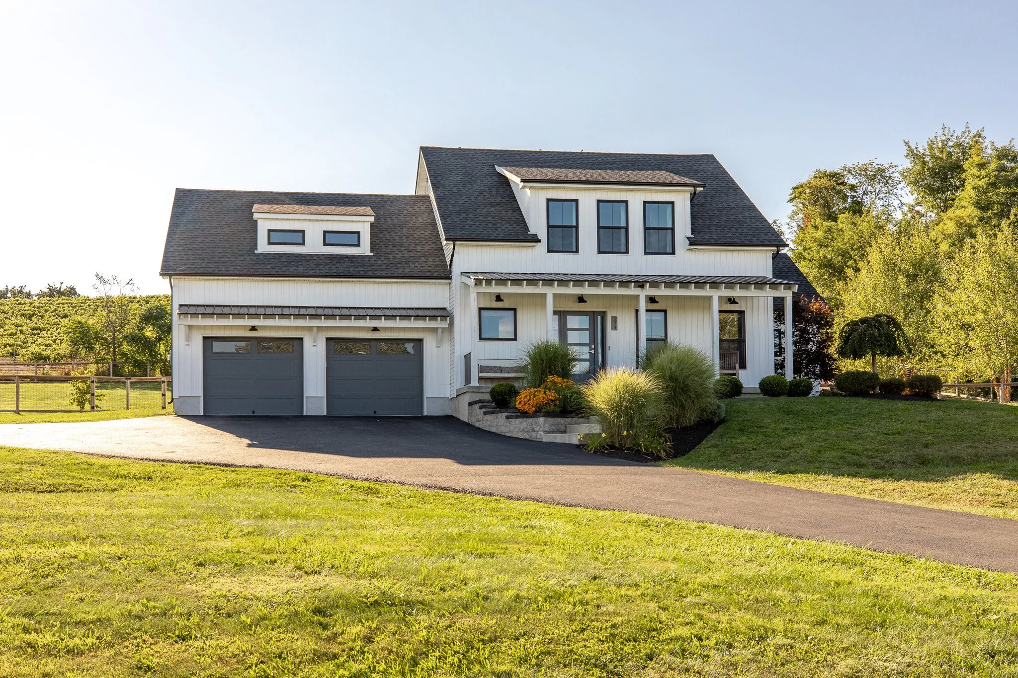 A modern two-story house with a gray roof and white exterior, surrounded by a lush green lawn and landscaped garden.