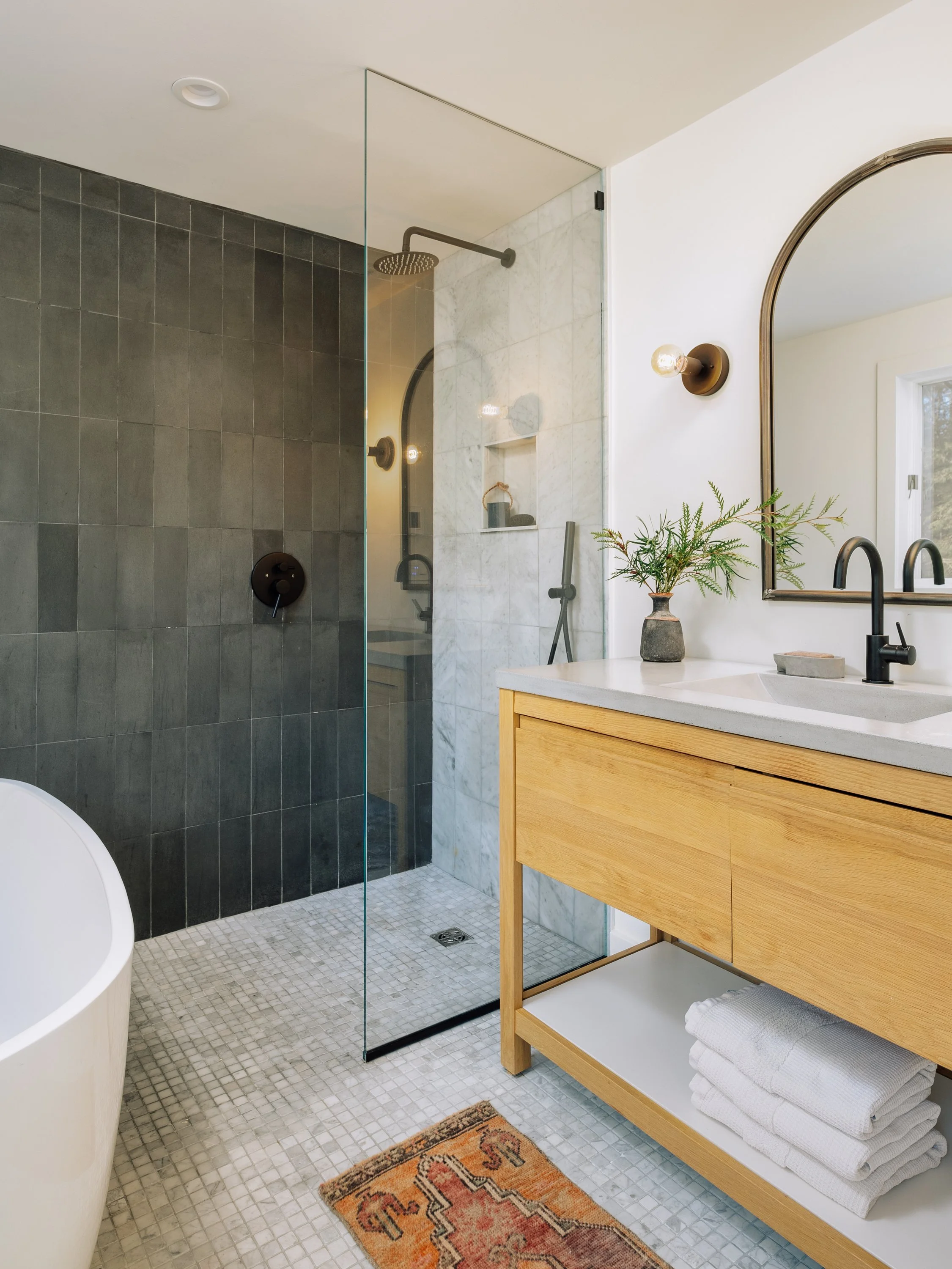 Modern bathroom with walk-in shower, wooden vanity with towels, mirror, and a window with natural light.