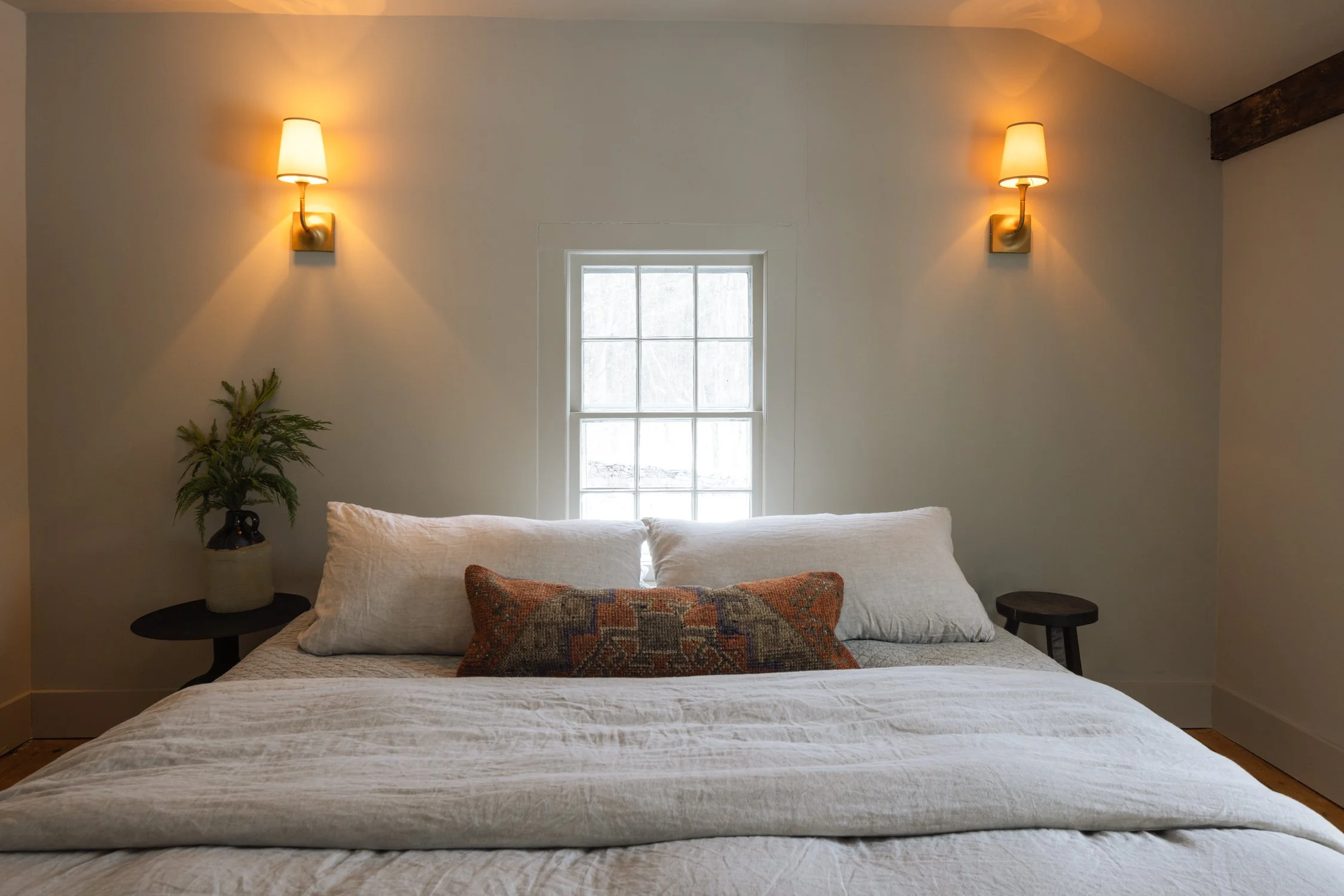A cozy bedroom with a bed, two nightstands, wall-mounted lamps, and a small window letting in natural light.