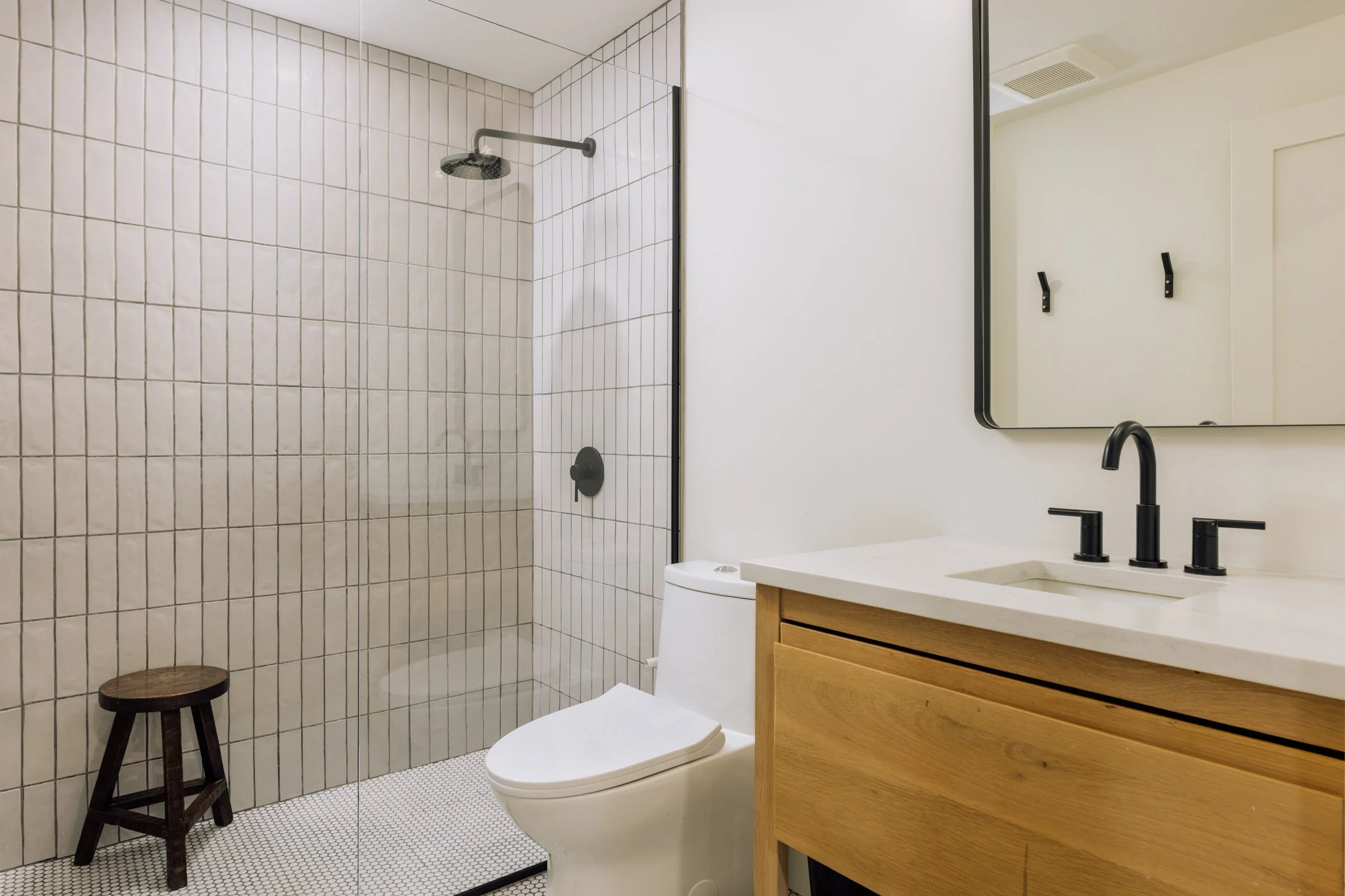 Modern bathroom with a walk-in shower, toilet, wooden vanity, black faucet, and a large mirror.