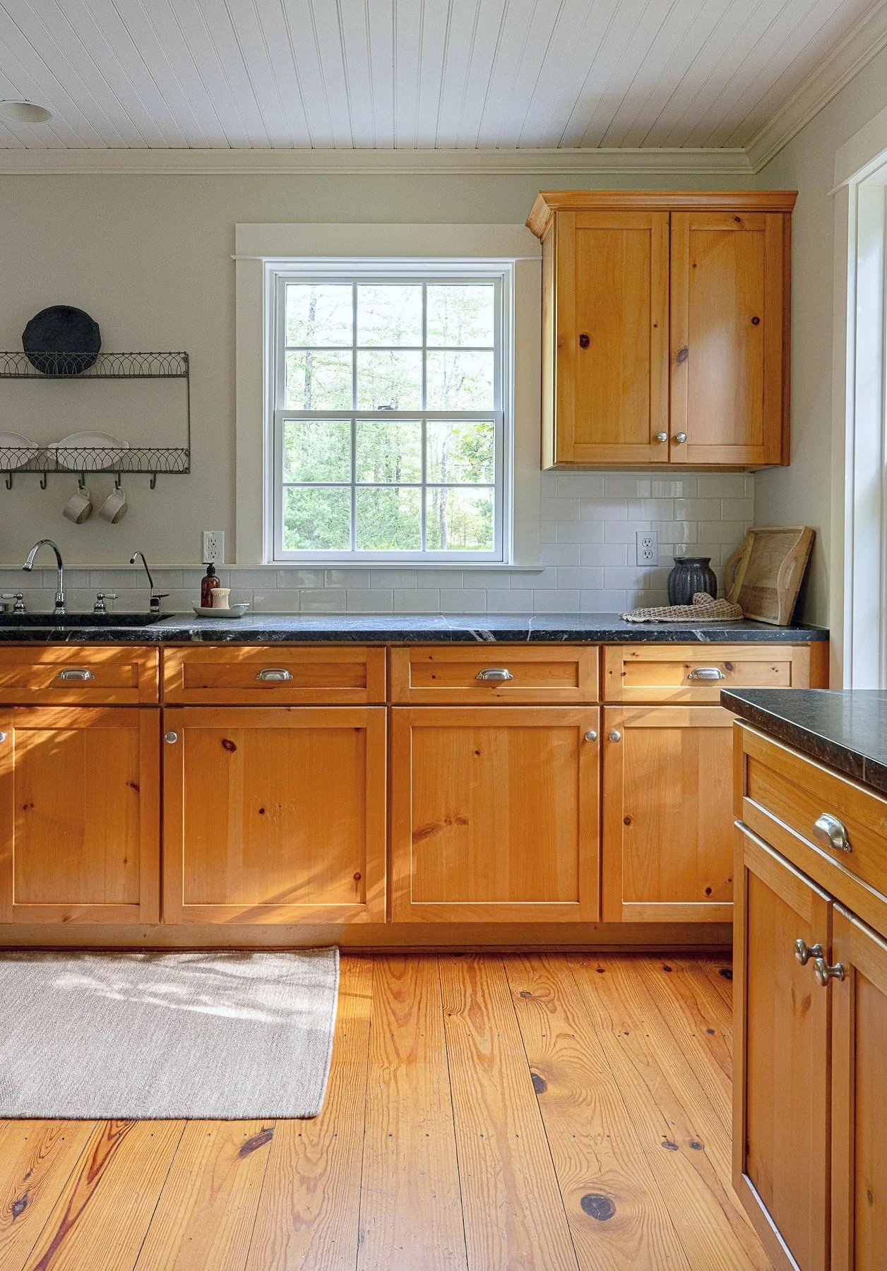 Kitchen with natural wood cabinets, a black countertop, a window, a double sink, and some decor on the counter.