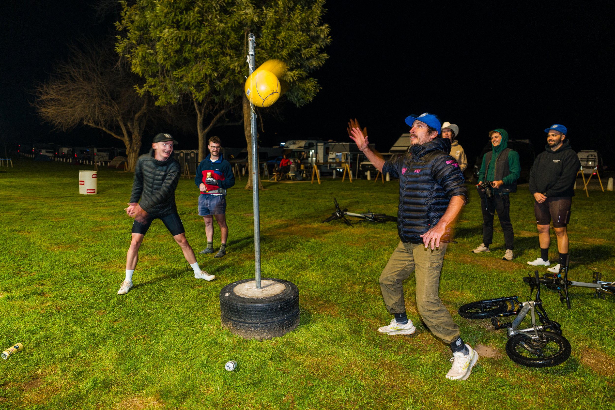 Group of cyclists at the start line of a gravel race, with a person dressed as a taco and a child with a taco accessory, under a banner that reads 'START' and 'FINISH' for 'The Rock Cobble Gravel Party' event.
