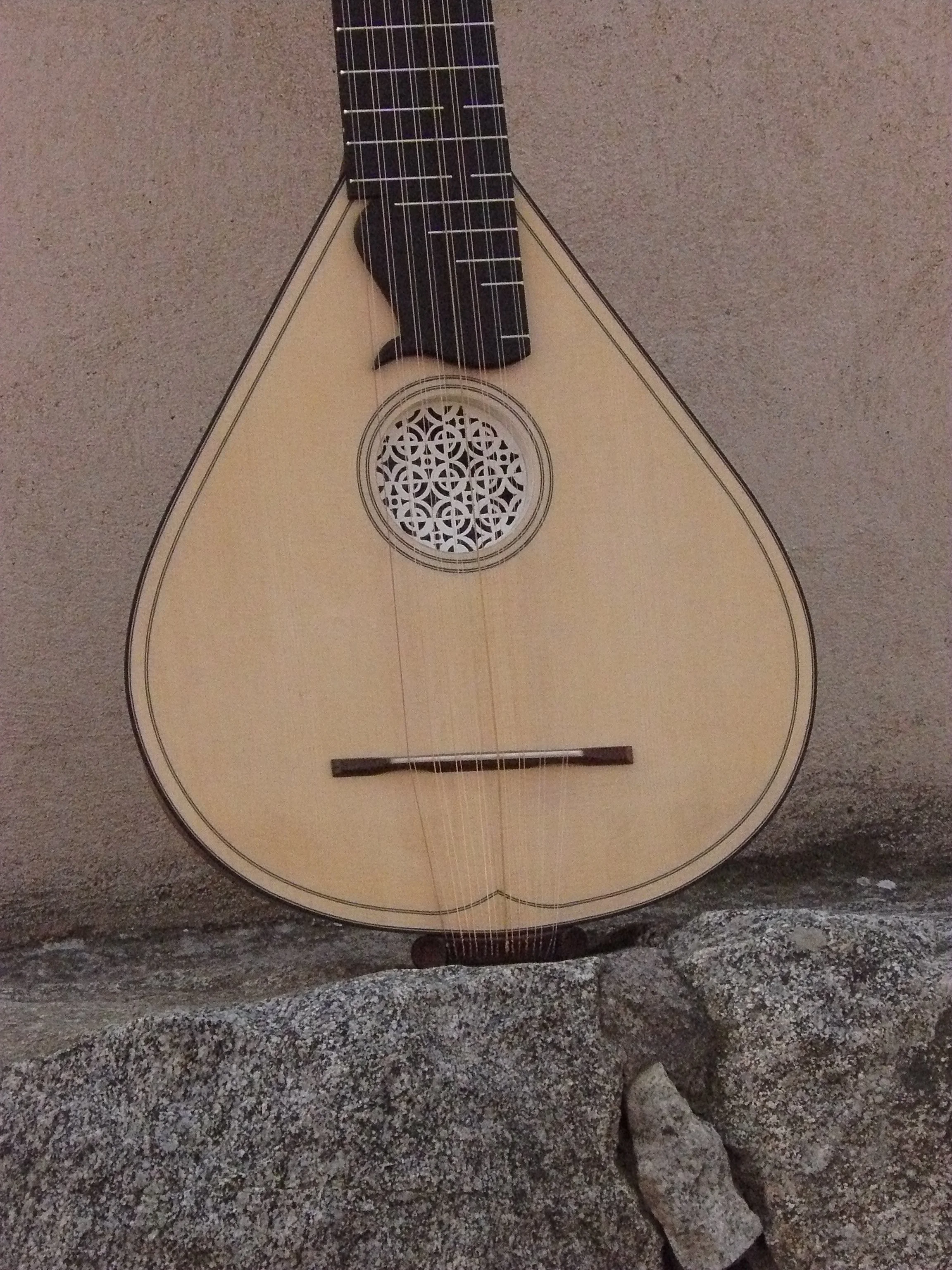 Une guitare acoustique de style oudoom repose contre un mur en pierre