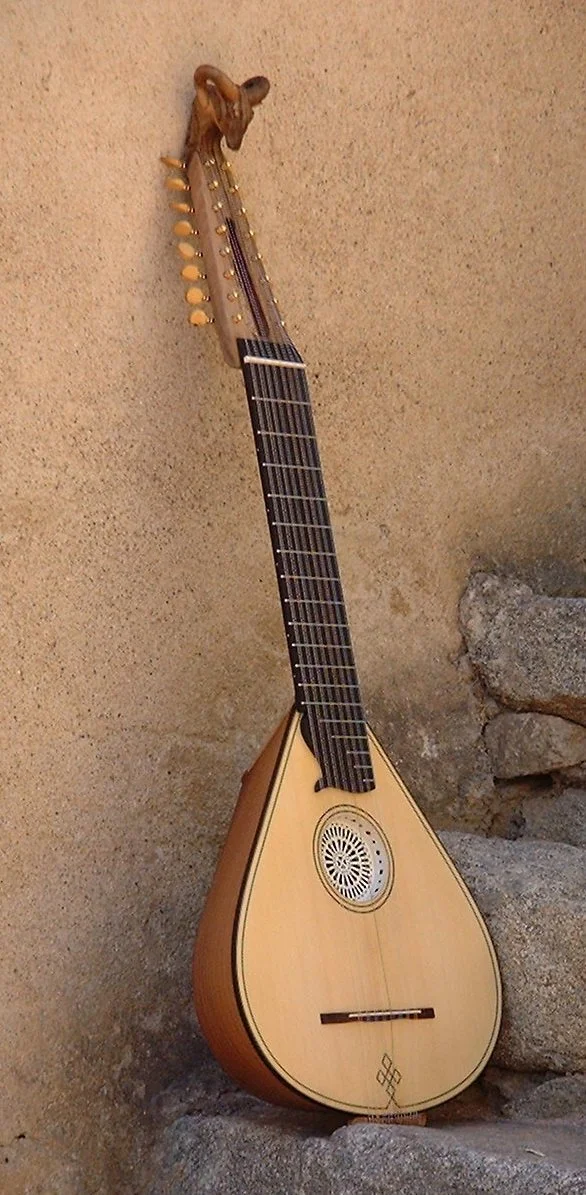 Une mandoline antique en bois avec des cordes, une rosace décorative et un manche long, posée contre un mur en pierre.