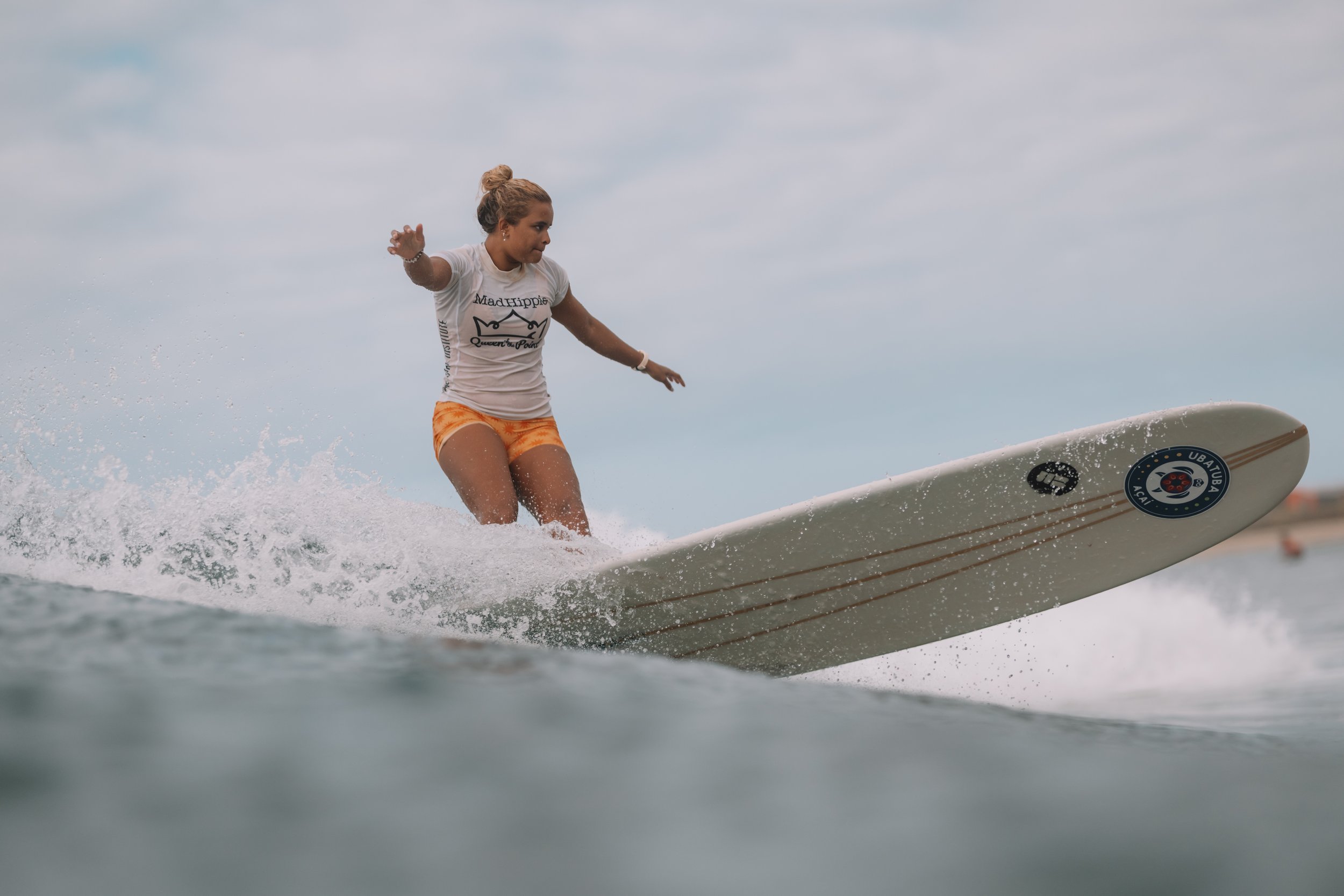 Young woman surfing on a wave with a cloudy sky background.
