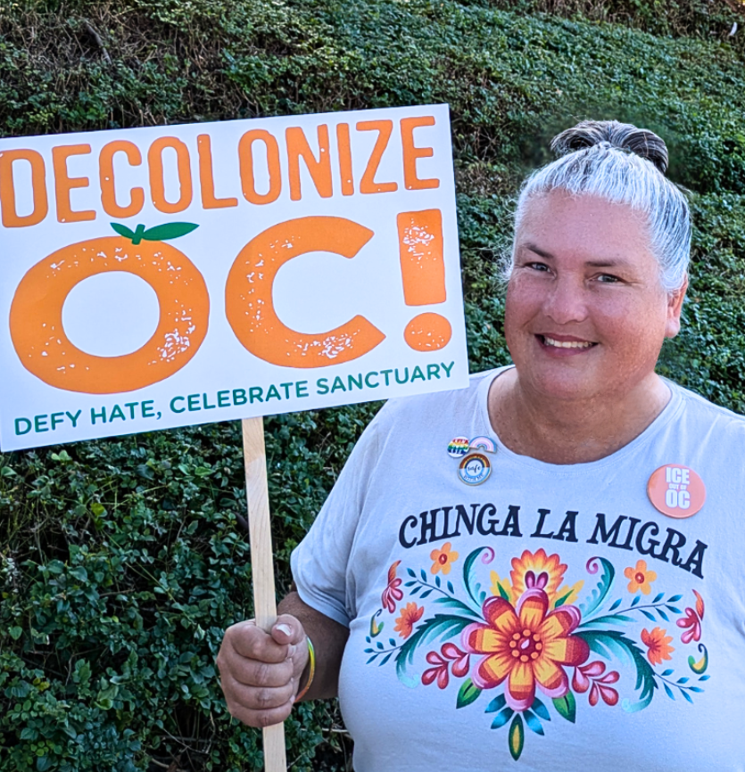 Amy Stevens wearing Chinga la Migra shirt and carrying Decolonize OC sign