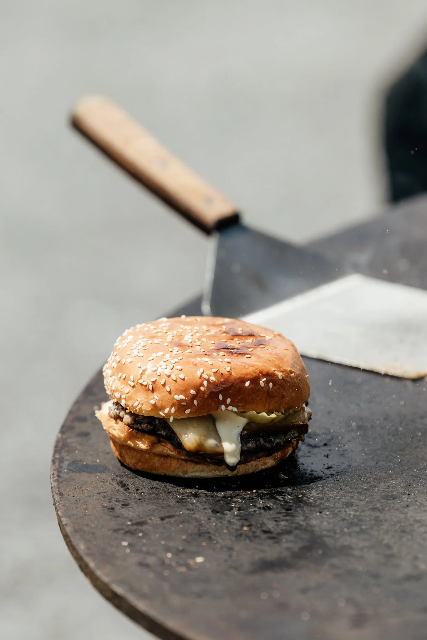 A cheeseburger with melted cheese, pickles, and a sesame seed bun on a black round surface.