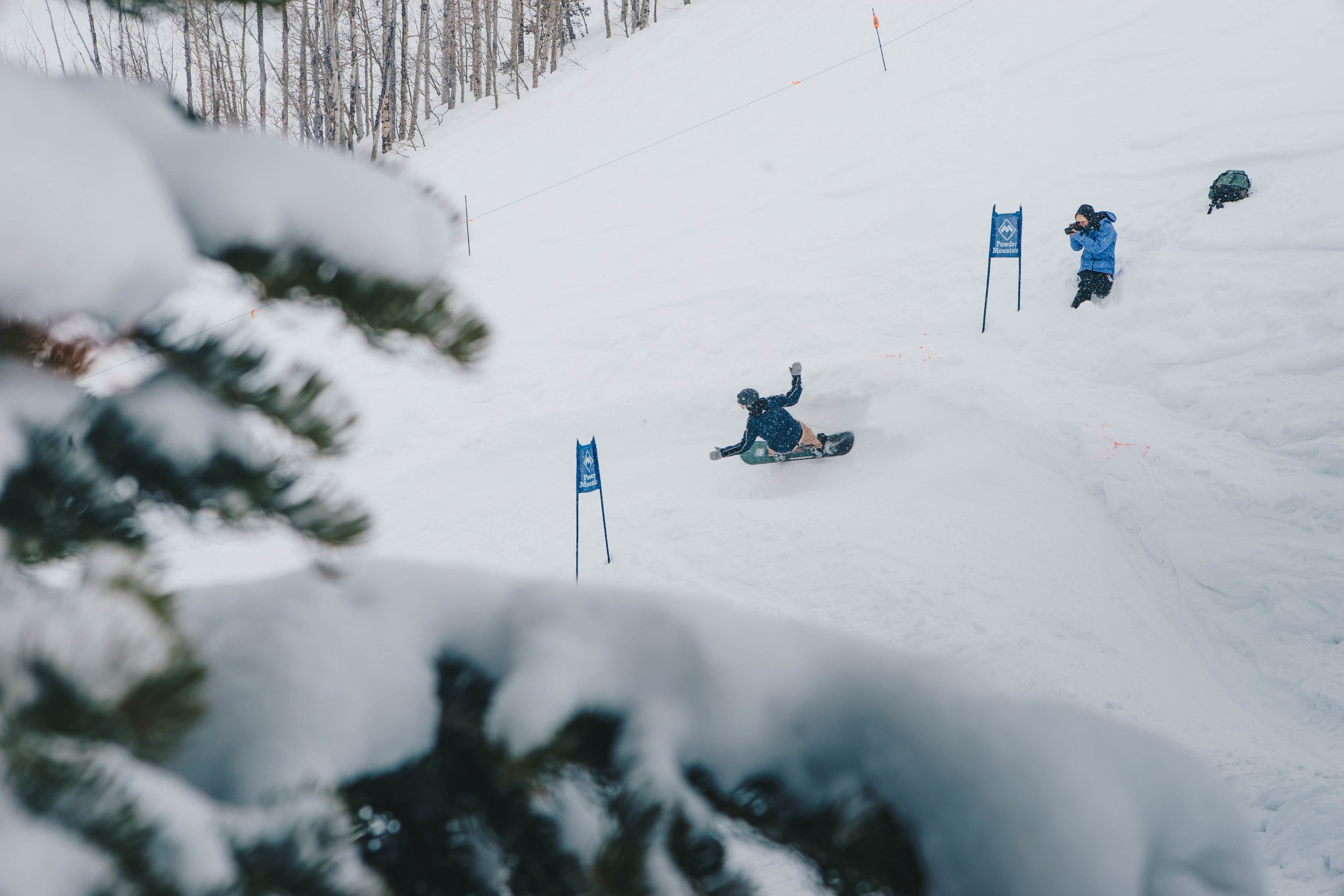 Snowboarder on a snowy slope, competing in a slalom race, with a photographer capturing the action.
