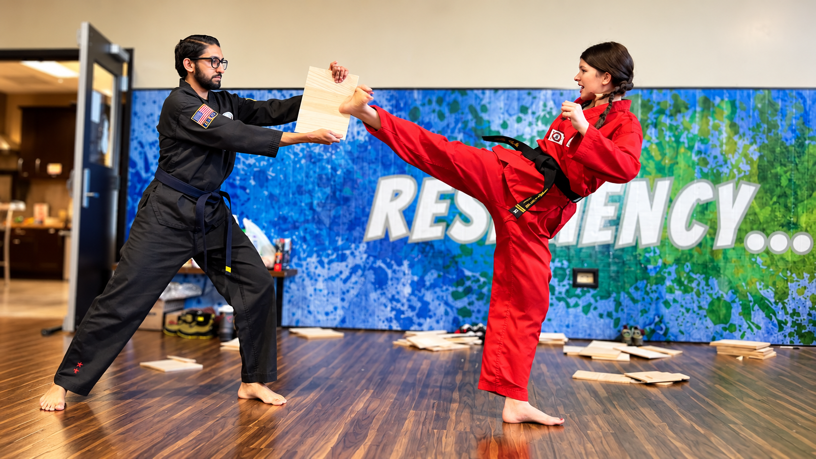 P.S. Academy Tae Kwon Do student practices a high kick against a board held by her instructor, demonstrating focus, confidence, and determination.