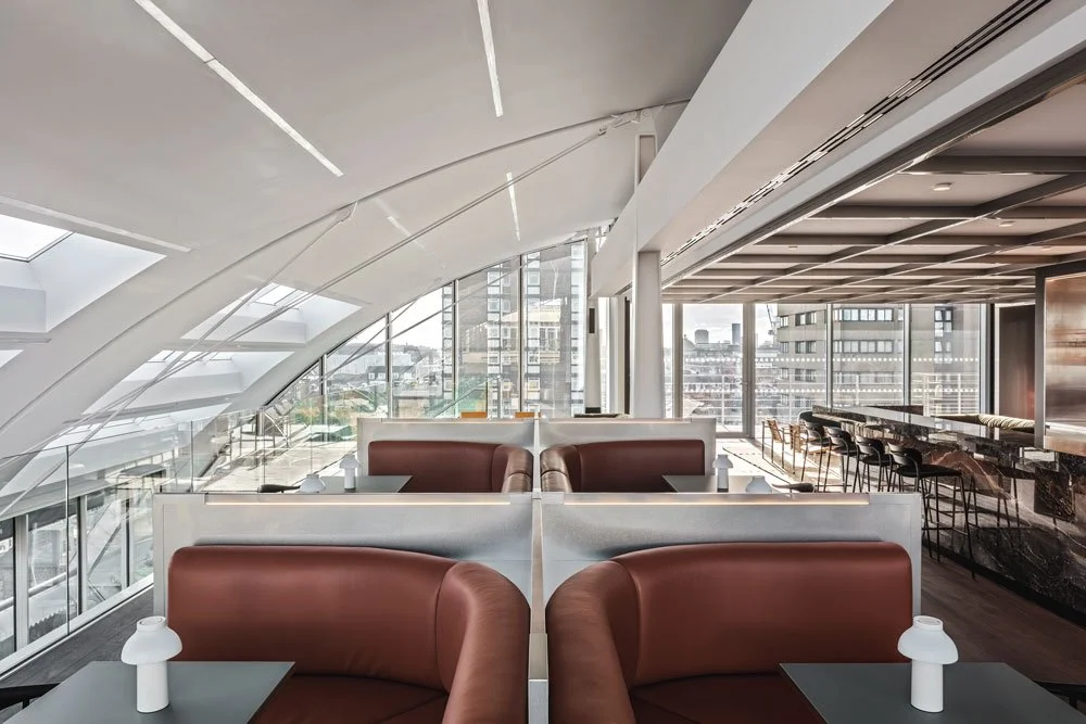 Modern, upscale office lounge with curved ceilings, large windows, white partitions, and brown leather chairs.