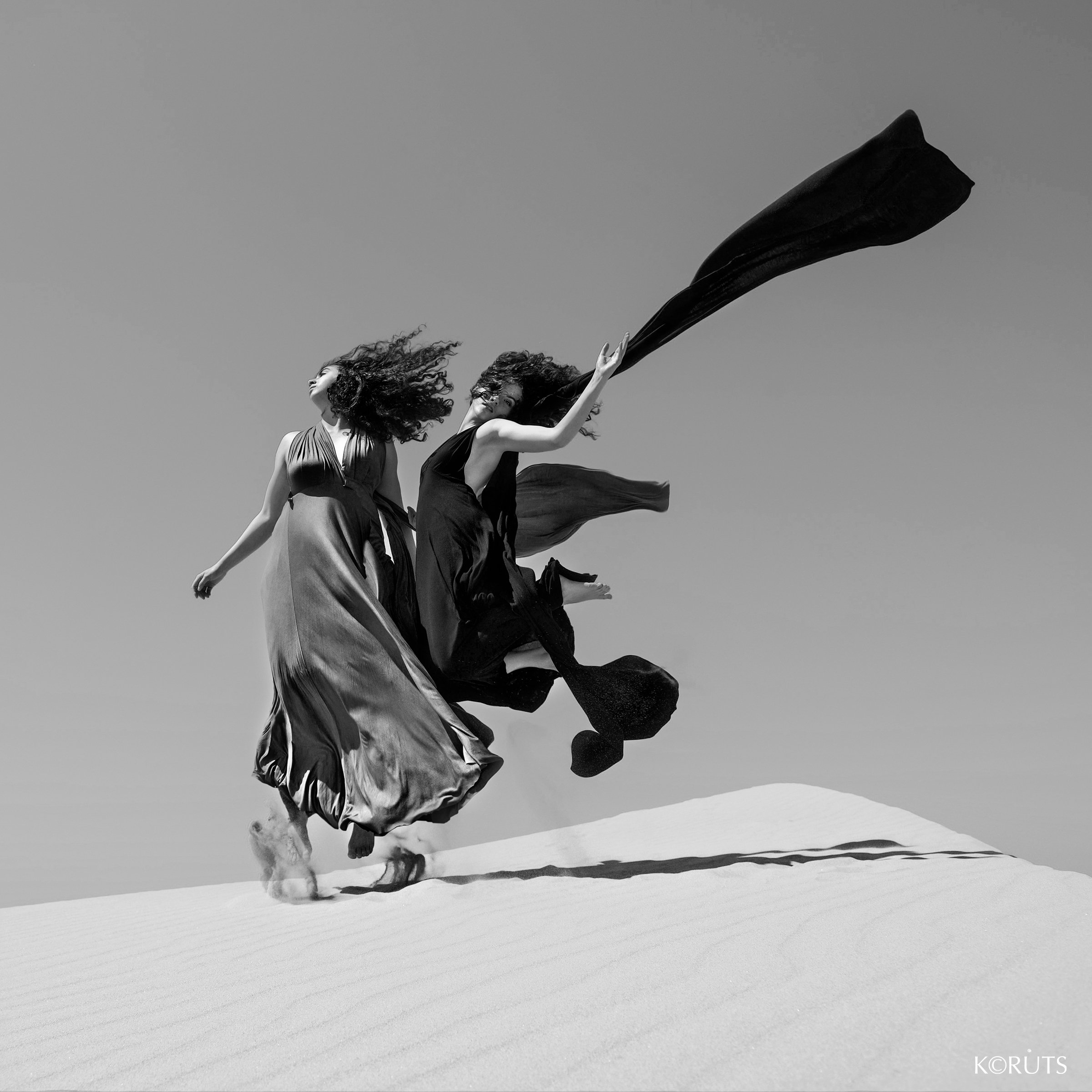 dramatic jump from two women in flowing dresses in the sand dunes