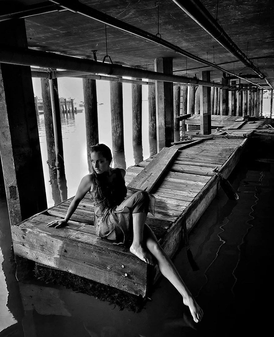 Black and white photo of a Ventura woman in a dress and bare feet under a pier