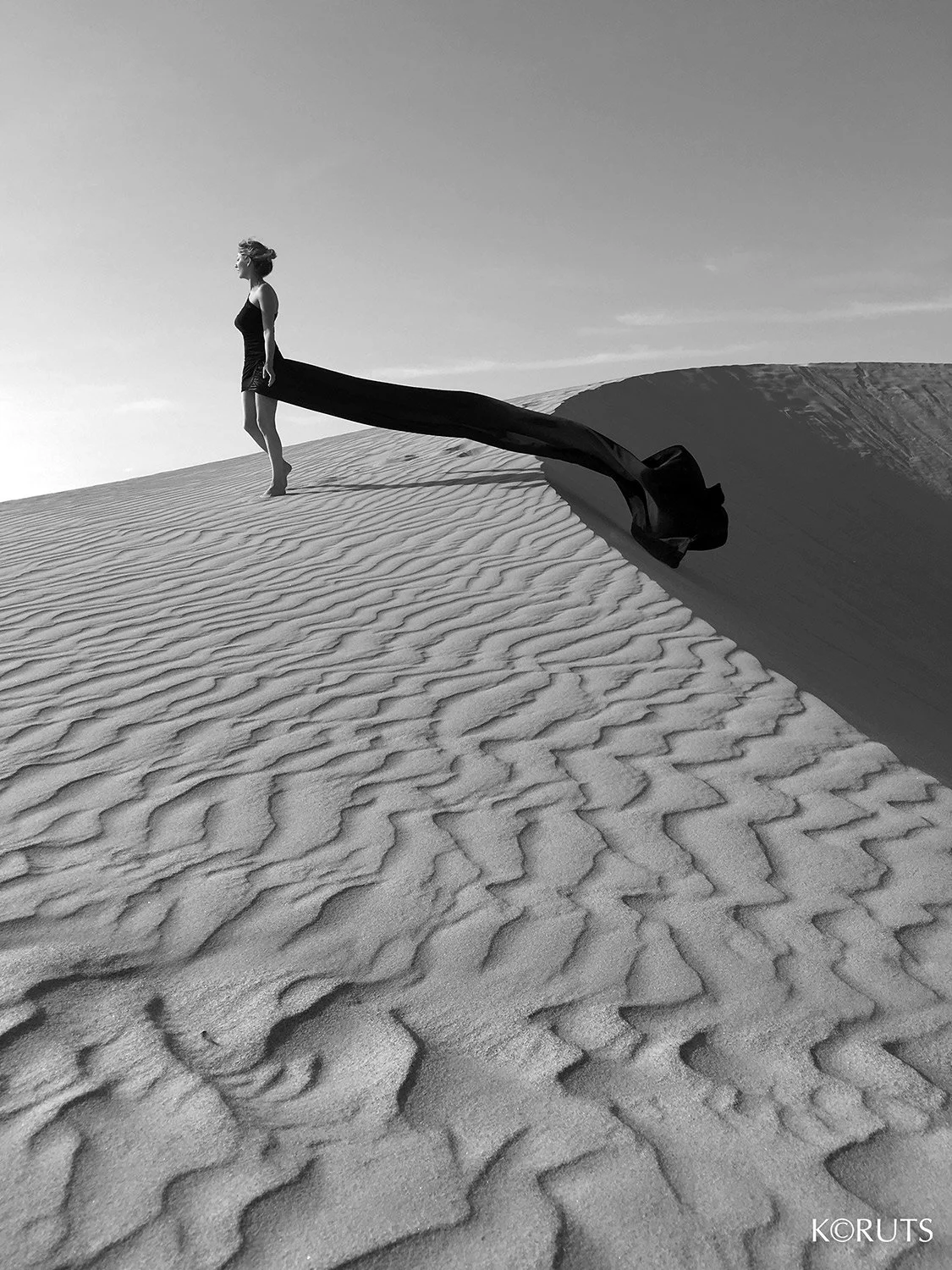 Woman standing on the edge of the dunes in black flowy dress