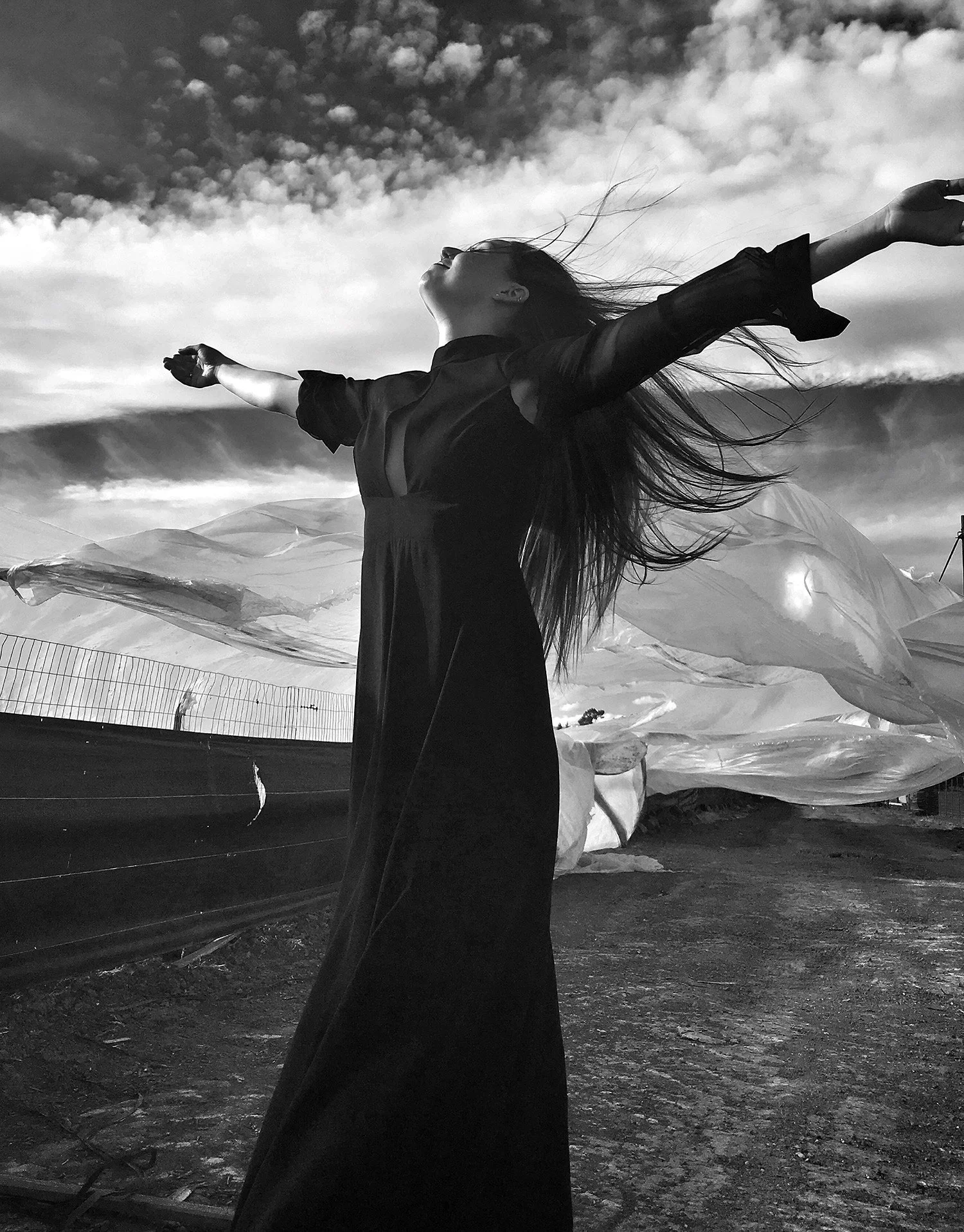 Black and white photo of a woman in black dress with arms stretched out to the sky