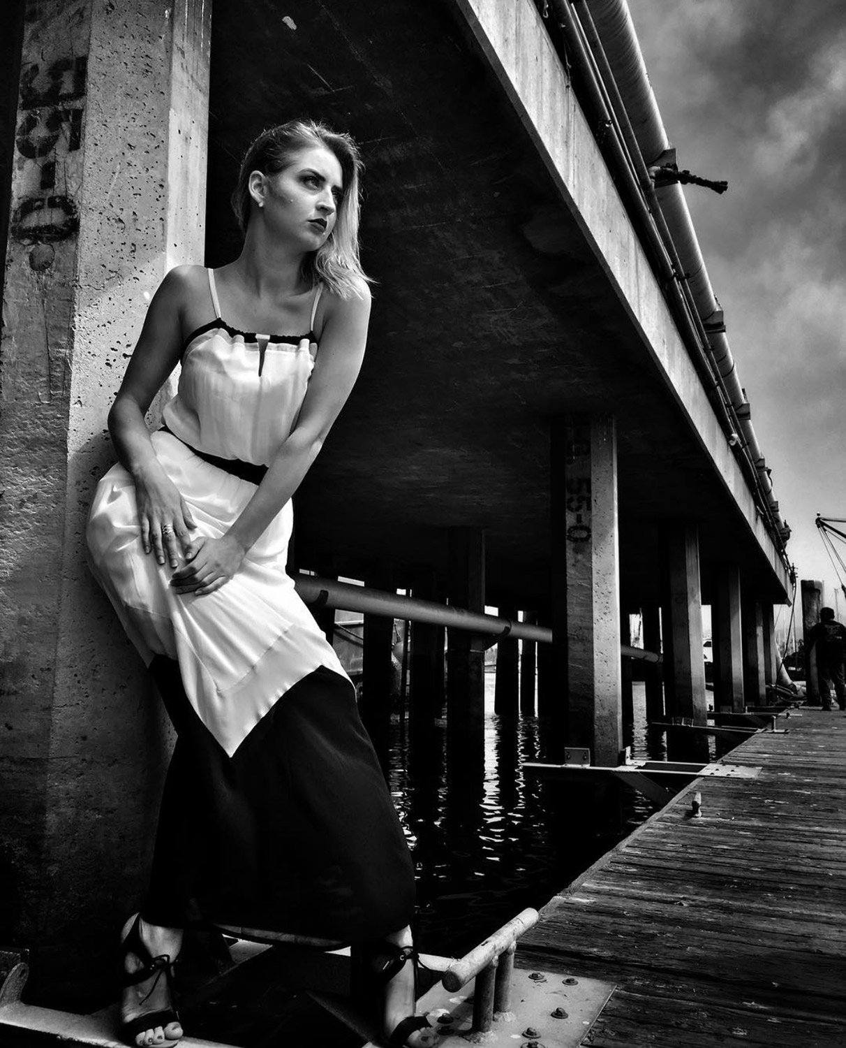 Black and white photo of a woman in a white dress on the pier looking out into the distance