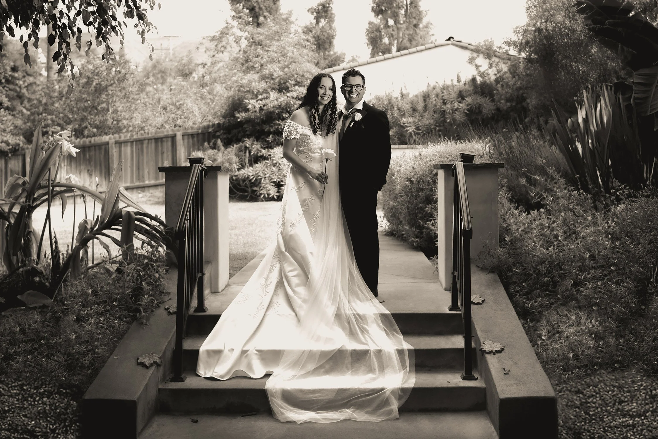 A happy couple with beaming smiles gets their portrait taken in the Church garden