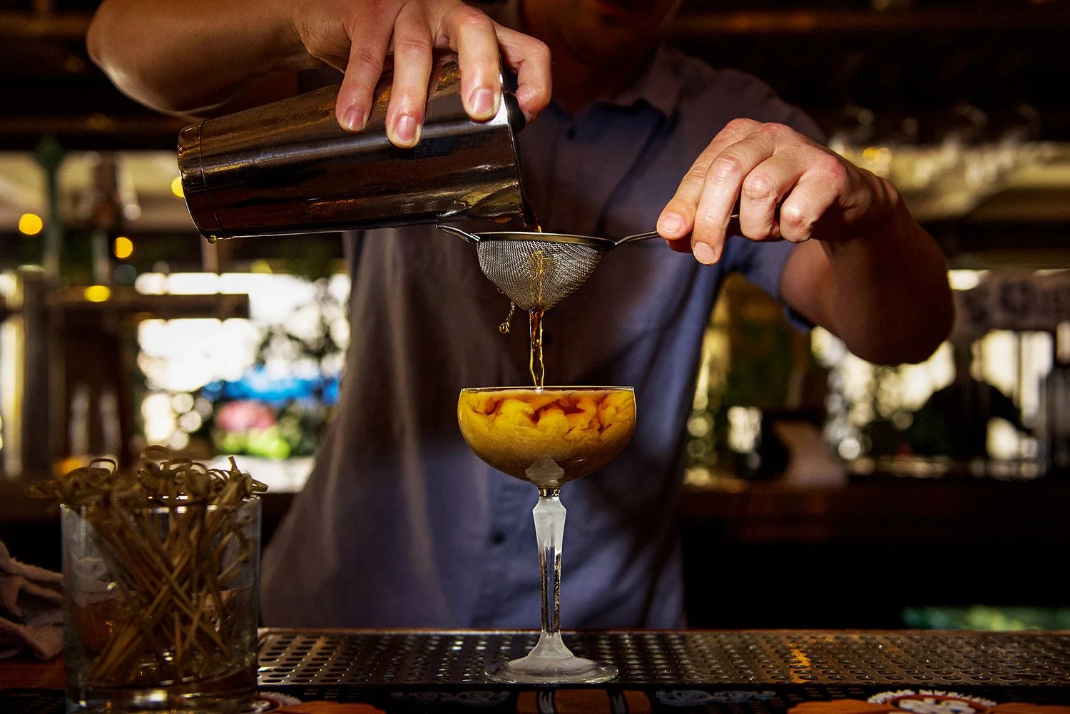 a bartender strains a handcrafted martini
