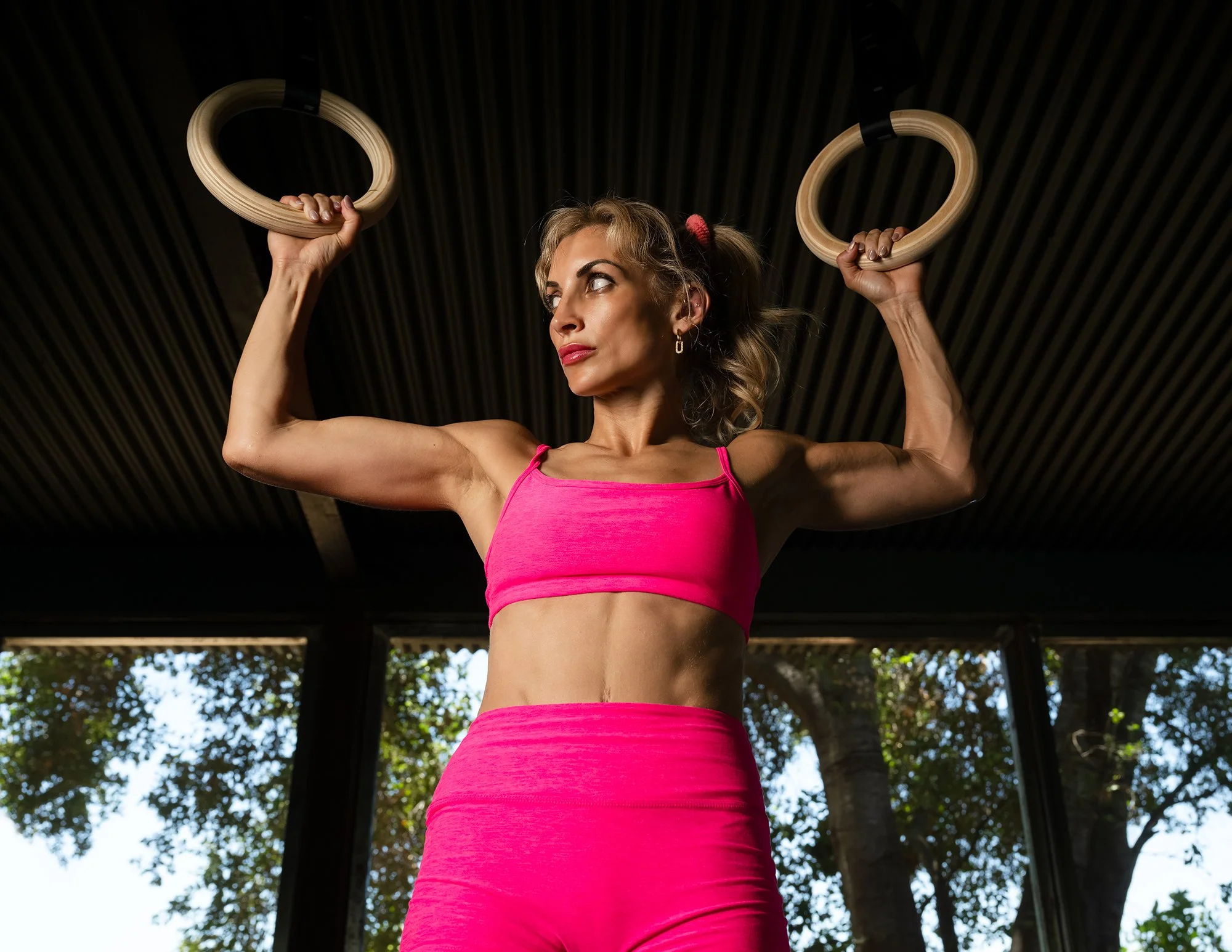 Athletic woman demonstrating upper body strength while hanging from gymnastic O-rings in a modern fitness studio.
