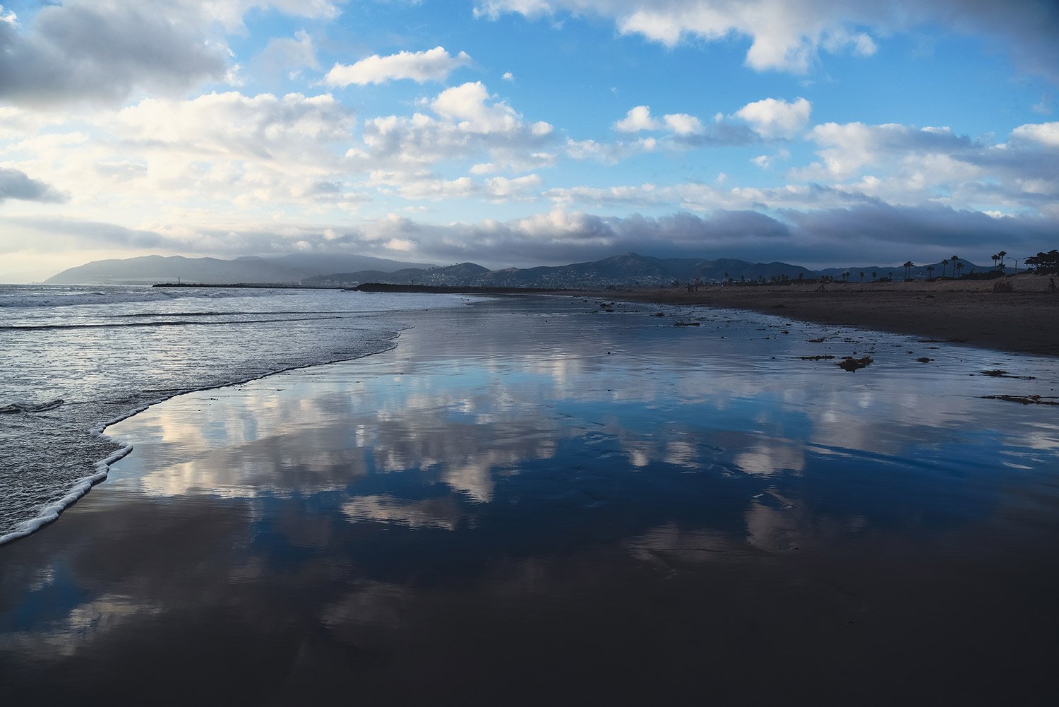 Ventura beach and a wet shore that reflects the blue and cloudy sky