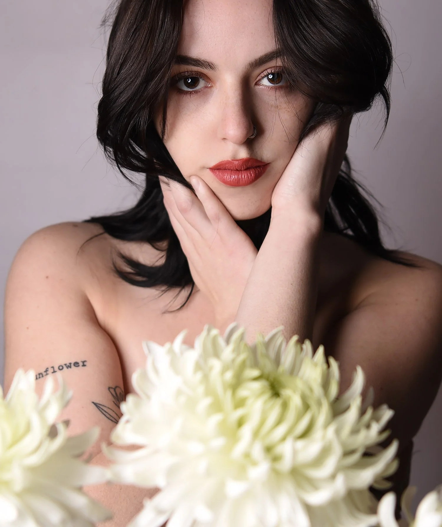 a young woman is posed behind a bouquet of flowers with her hand poised by her face