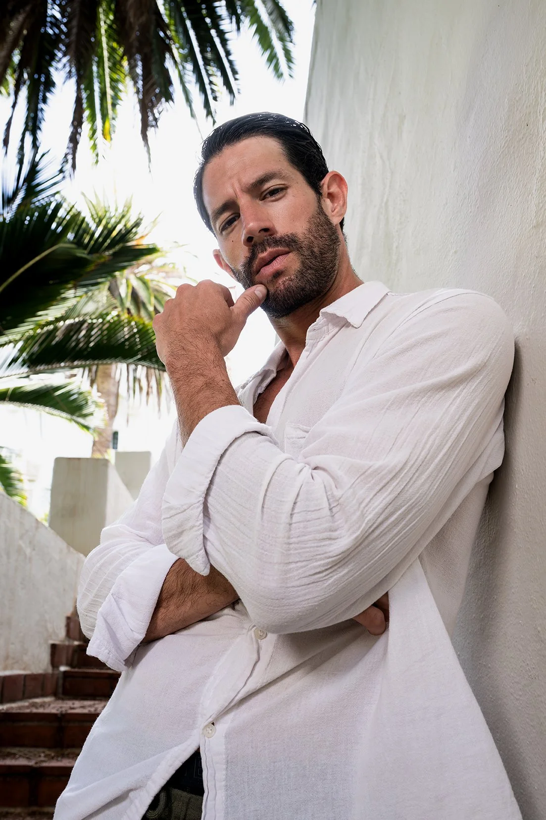Spanish male model wearing a relaxed-fit men's linen shirt, posing against rustic Spanish architecture for a menswear commercial ad campaign.