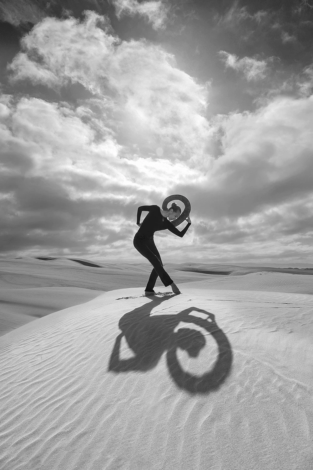 a black and white image of a woman casting a unique shadow in dunes