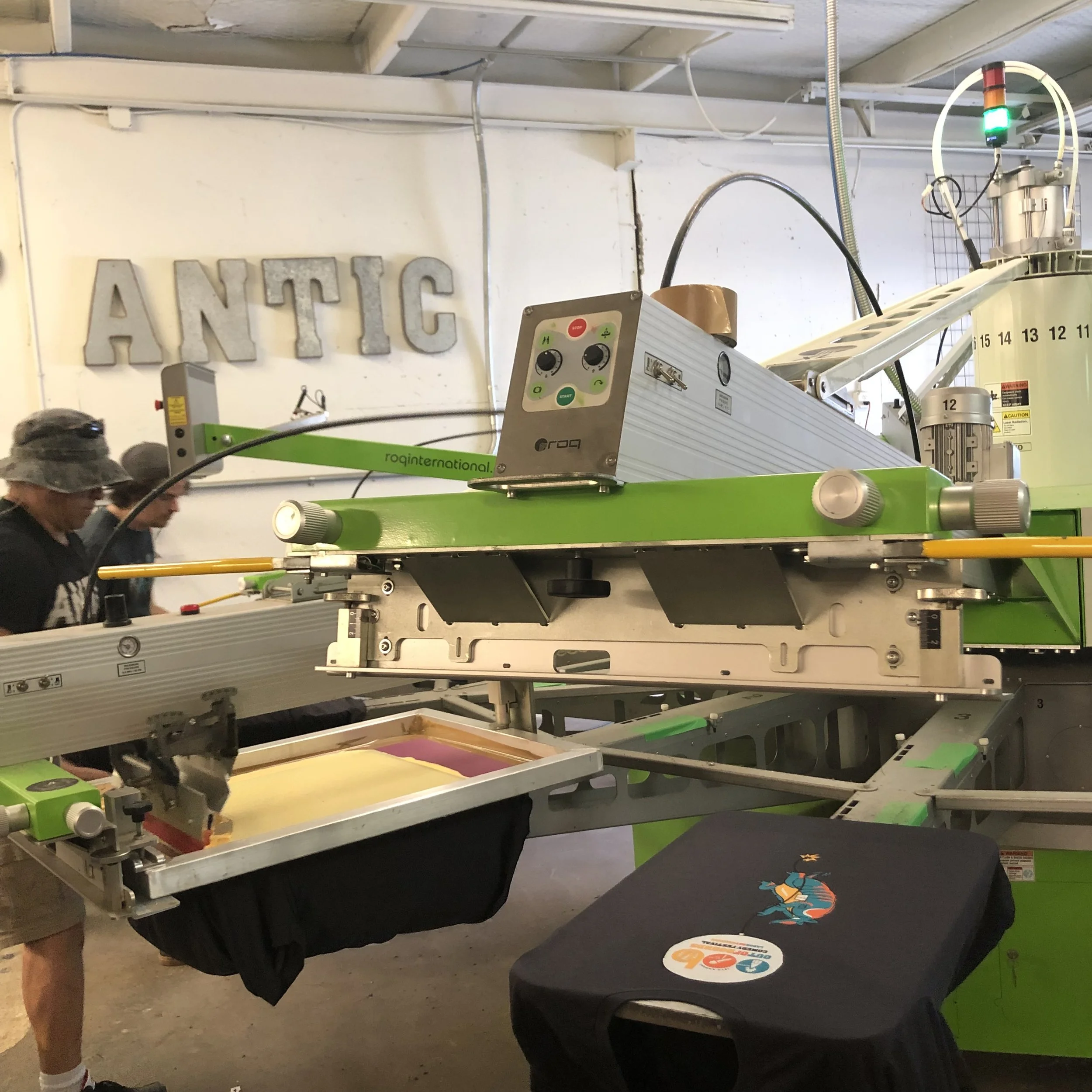 Screen printing press with custom shirt being printed by two men in hats. 