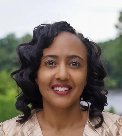 Headshot of Kibri Everett smiling outdoors with trees and a body of water blurred in the background.