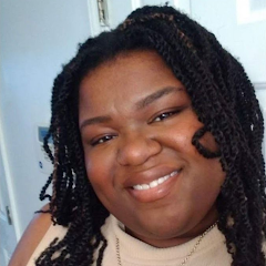 Headshot of Cat smiling, wearing a light-colored top and necklace, with locs framing her face.