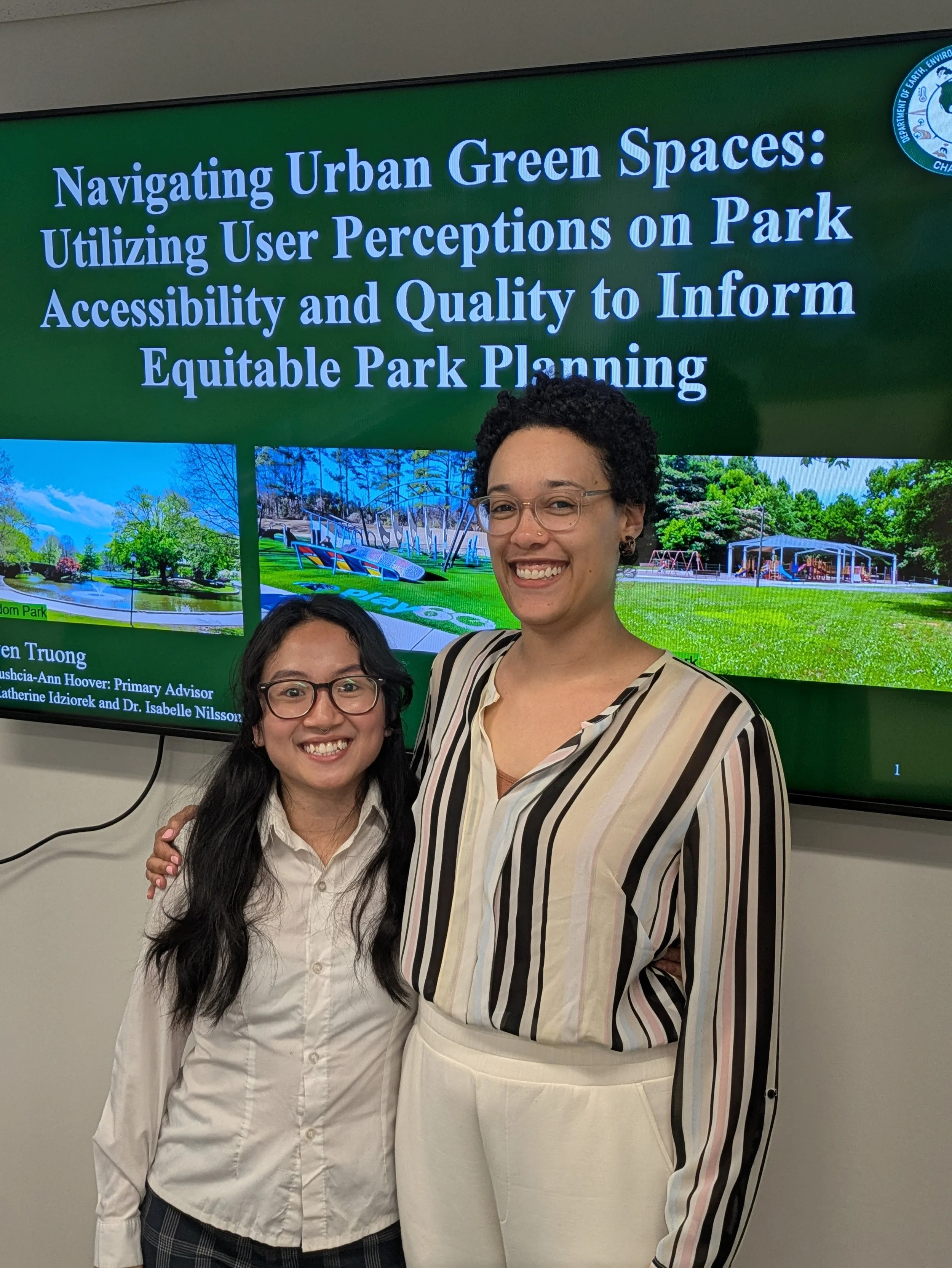 Dr. Hoover wears a multi-colored striped blouse and white pants, and stand next to Tuyen, who is dressed in a white blouse and black slacks. They both smile and pose for Tuyen's thesis defense.