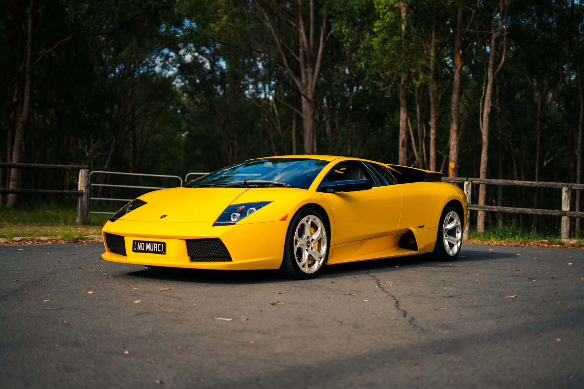A bright yellow Lamborghini sports car parked on an asphalt road surrounded by trees.