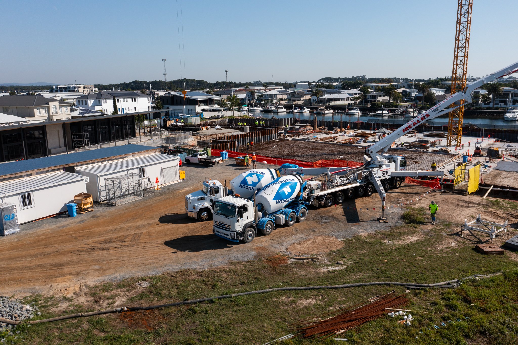 Construction site near a waterfront with concrete mixers, a crane, and workers.