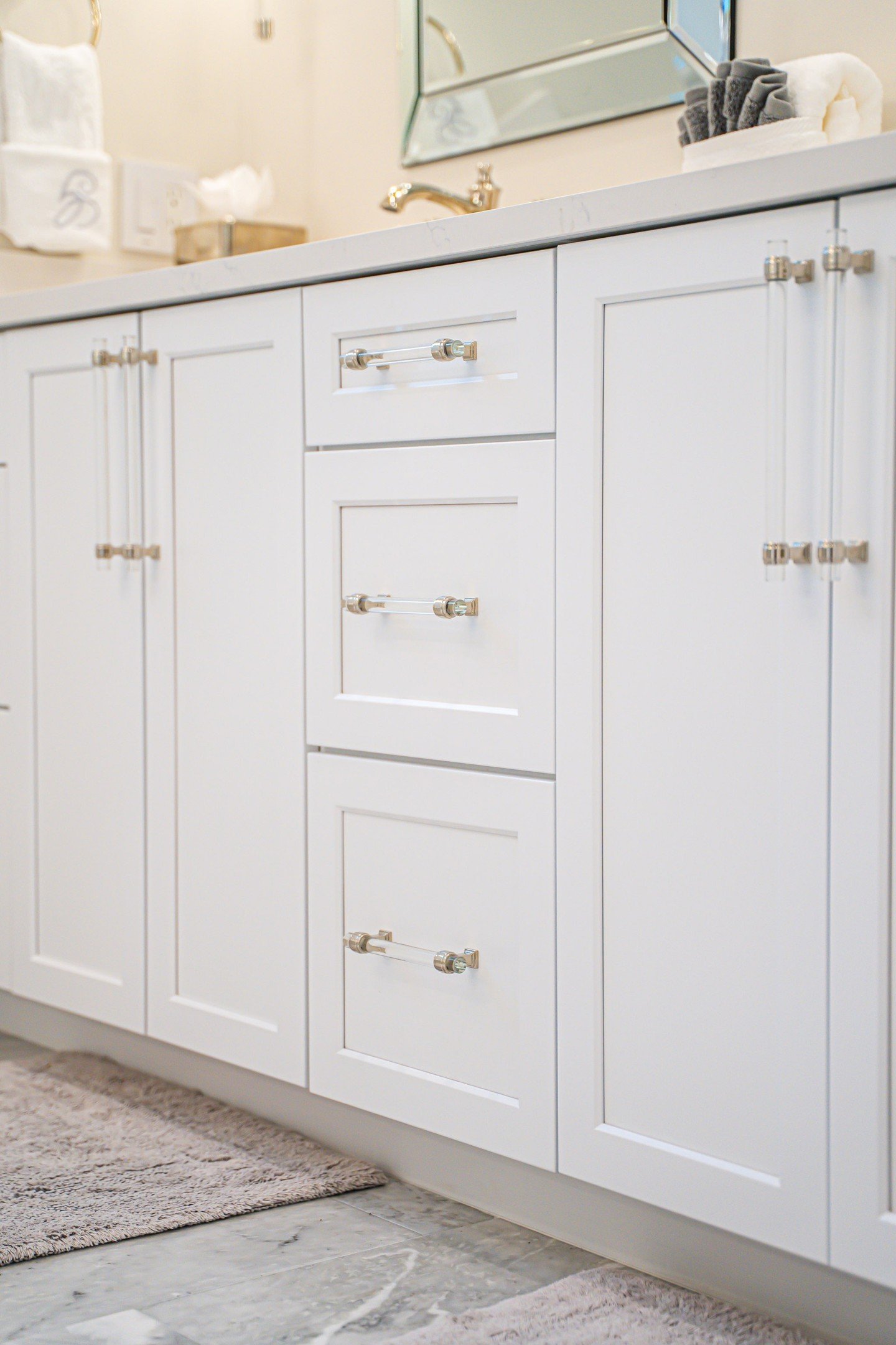 Loving this bright + elegant bathroom refresh  From the crisp white cabinetry and mirrored accents to the soft neutral tones and cozy textures.The gold hardware and wall sconces add just the right touch of warmth and luxury. #installedandloved🖤