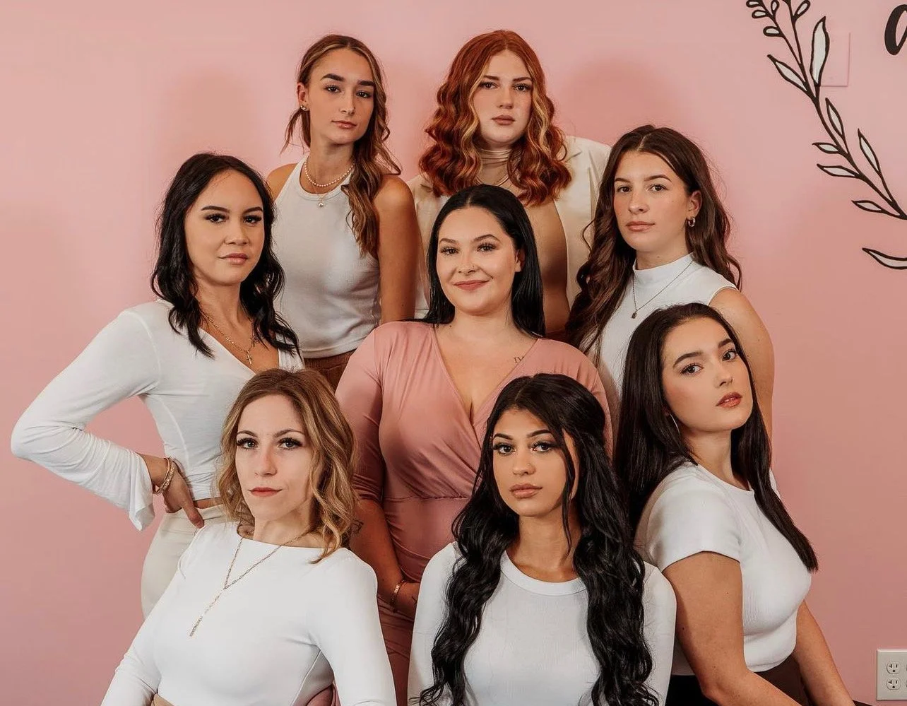 Group of ten women posing together against a pink background with black floral designs.