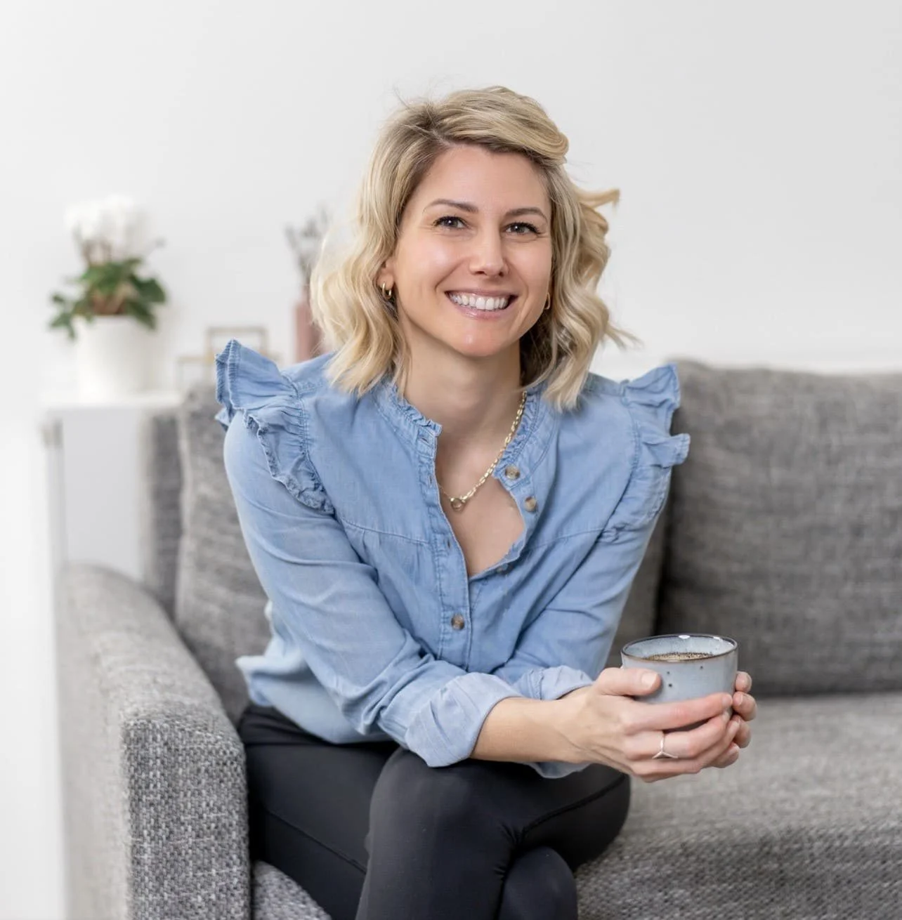 Photo of Rebecca Michelle, private meditation coach sitting on a couch smiling with a cup of tea in her hand.