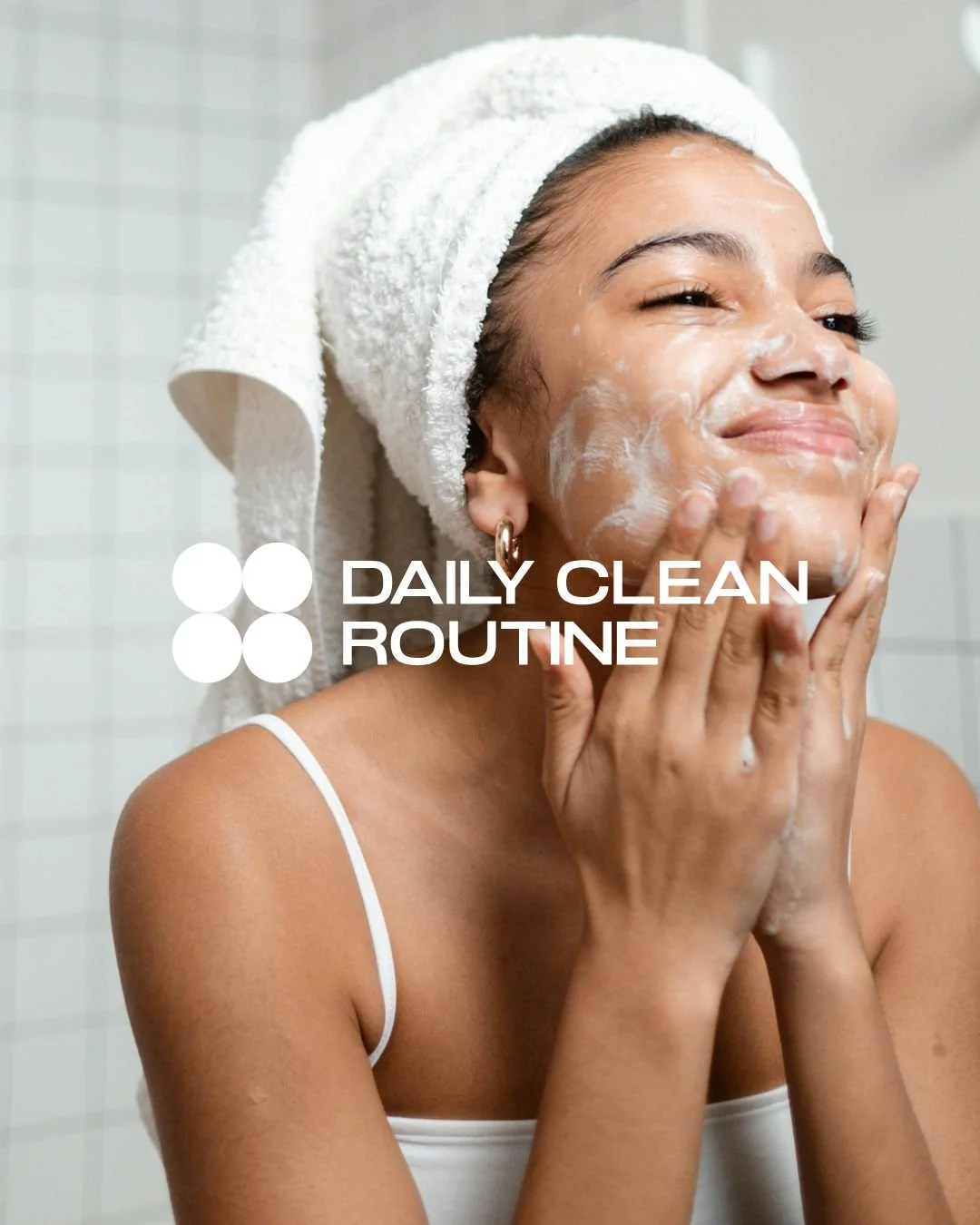 Image of a woman in the bathroom with a towel on her head washing her face with a foaming cleanser with the blue graphic logo of Daily Clean Routine layered on top