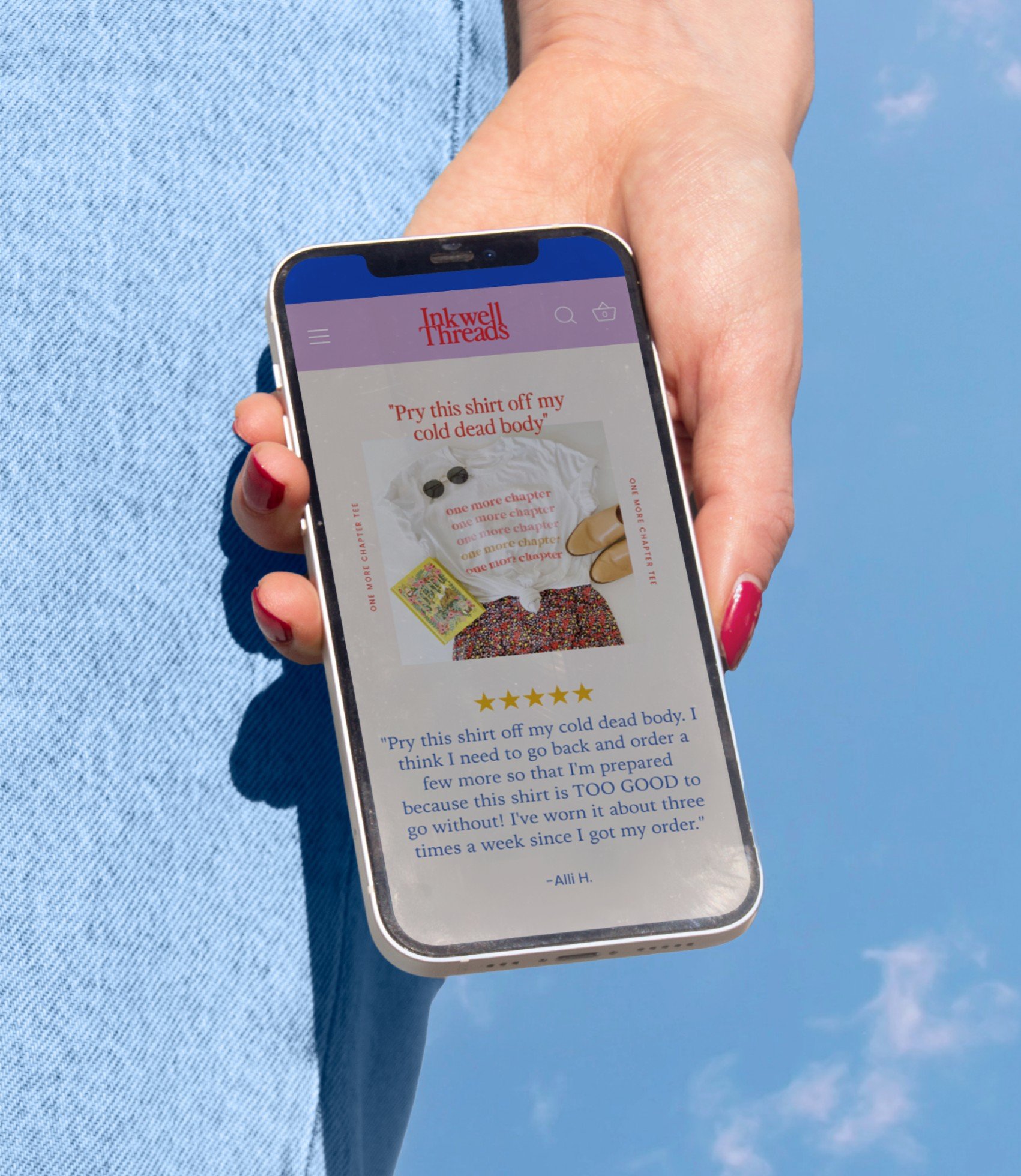 Hand holding phone with Inkwell Threads website in front of a blue sky background