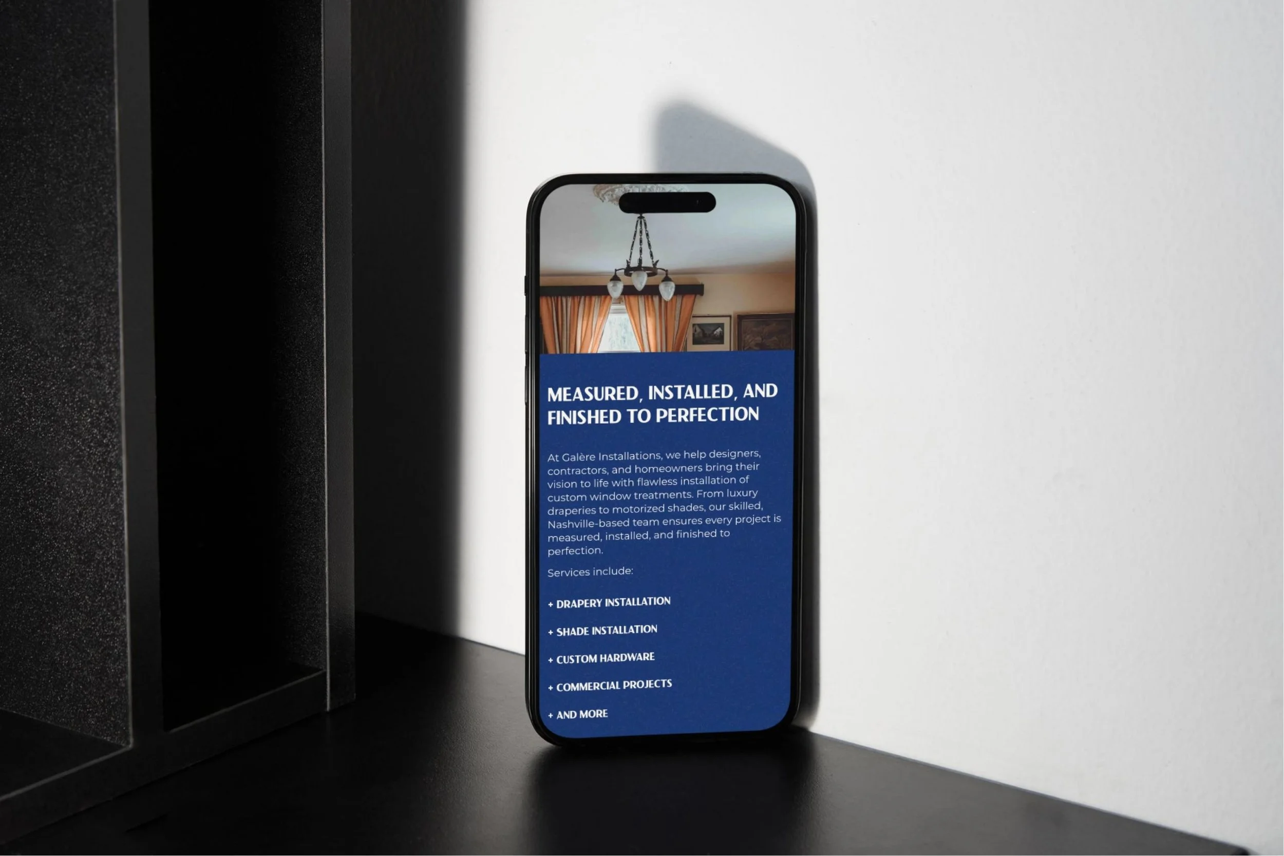 Phone against white wall with Galère installations website page in it