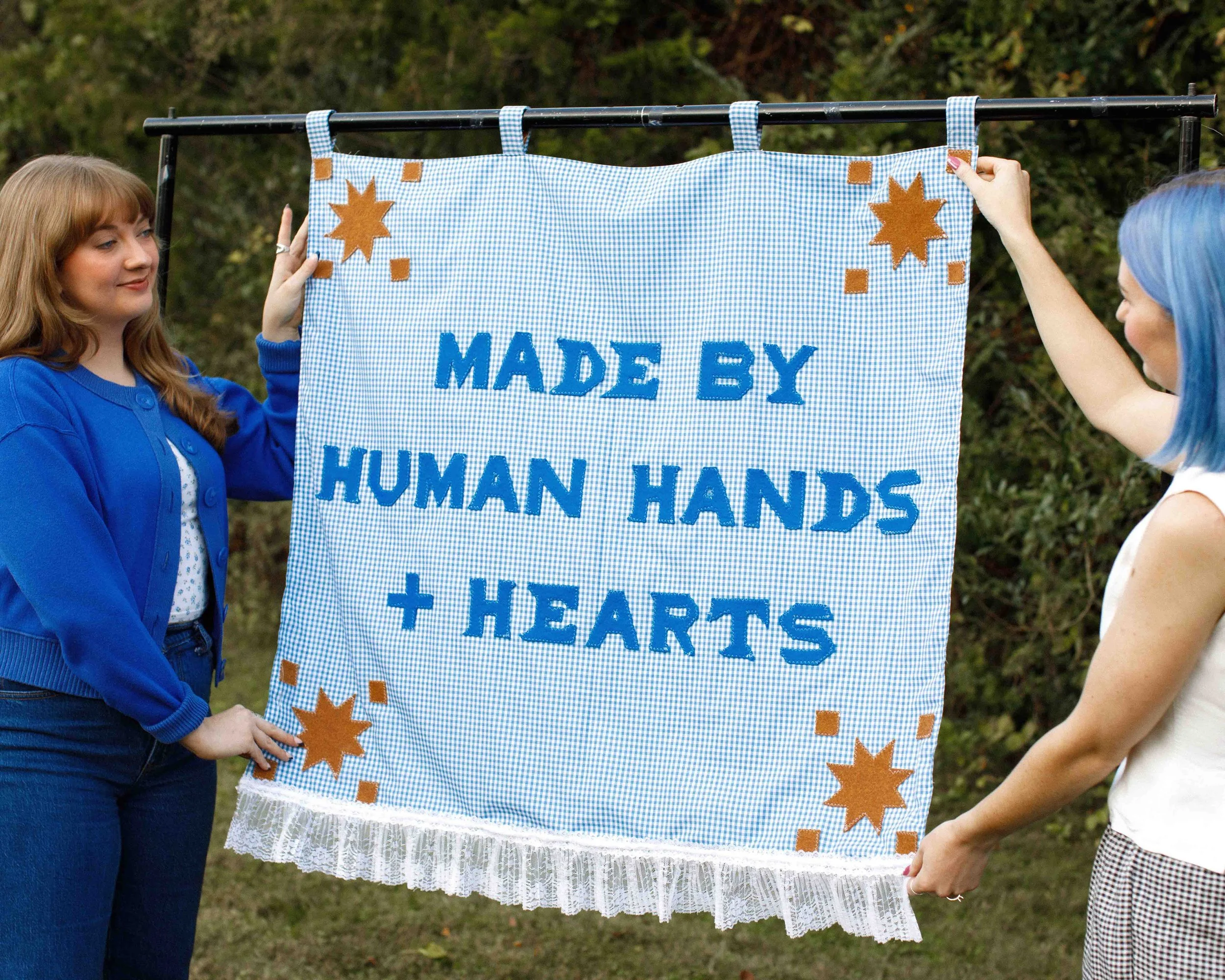 Foxtrot Branding cofounders Cass & Amanda holding blue banner that says "made by human hands + hearts"