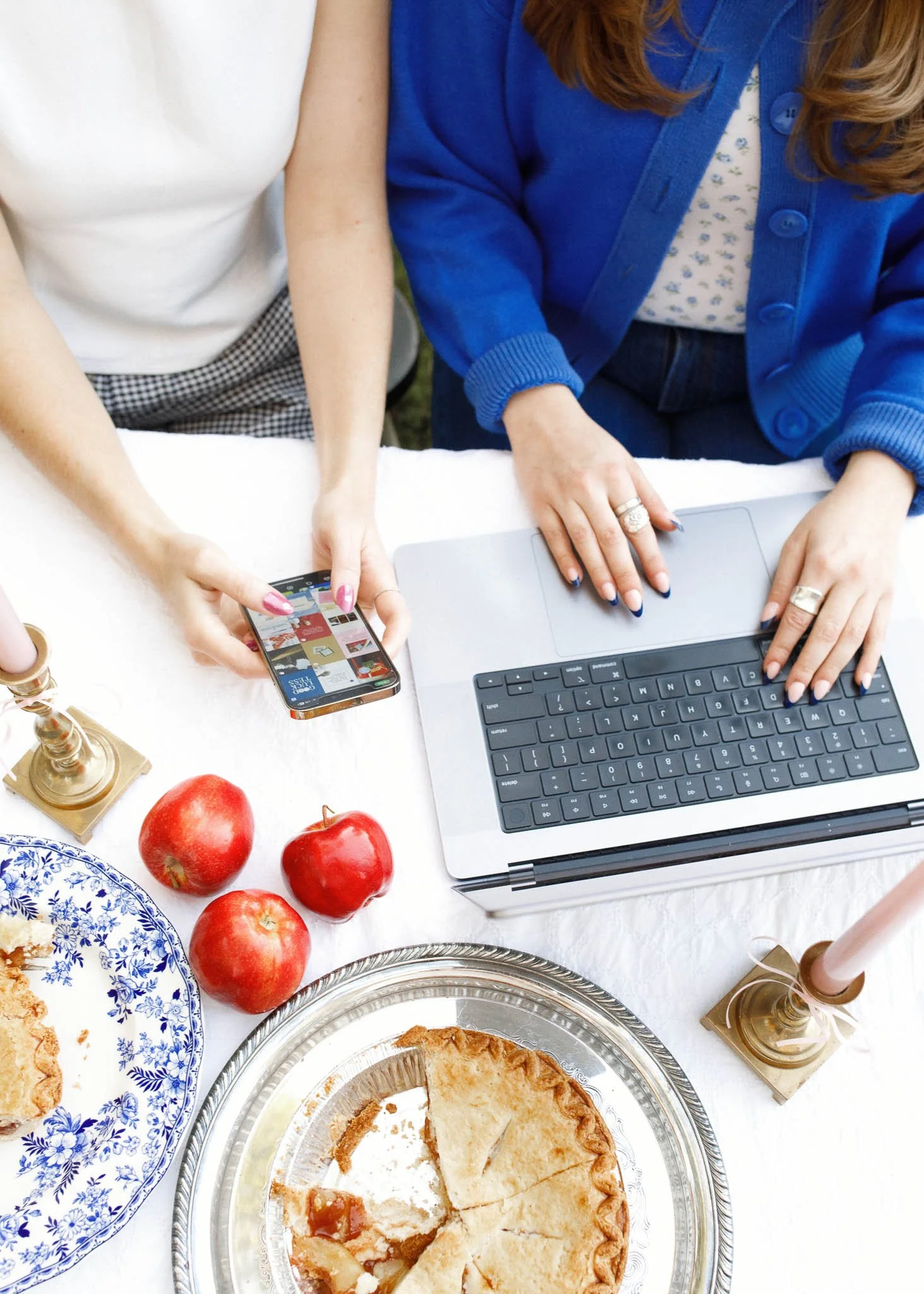 A top-down photo of a table with picnic items and a laptop with two sets of hands on laptop and holding phone