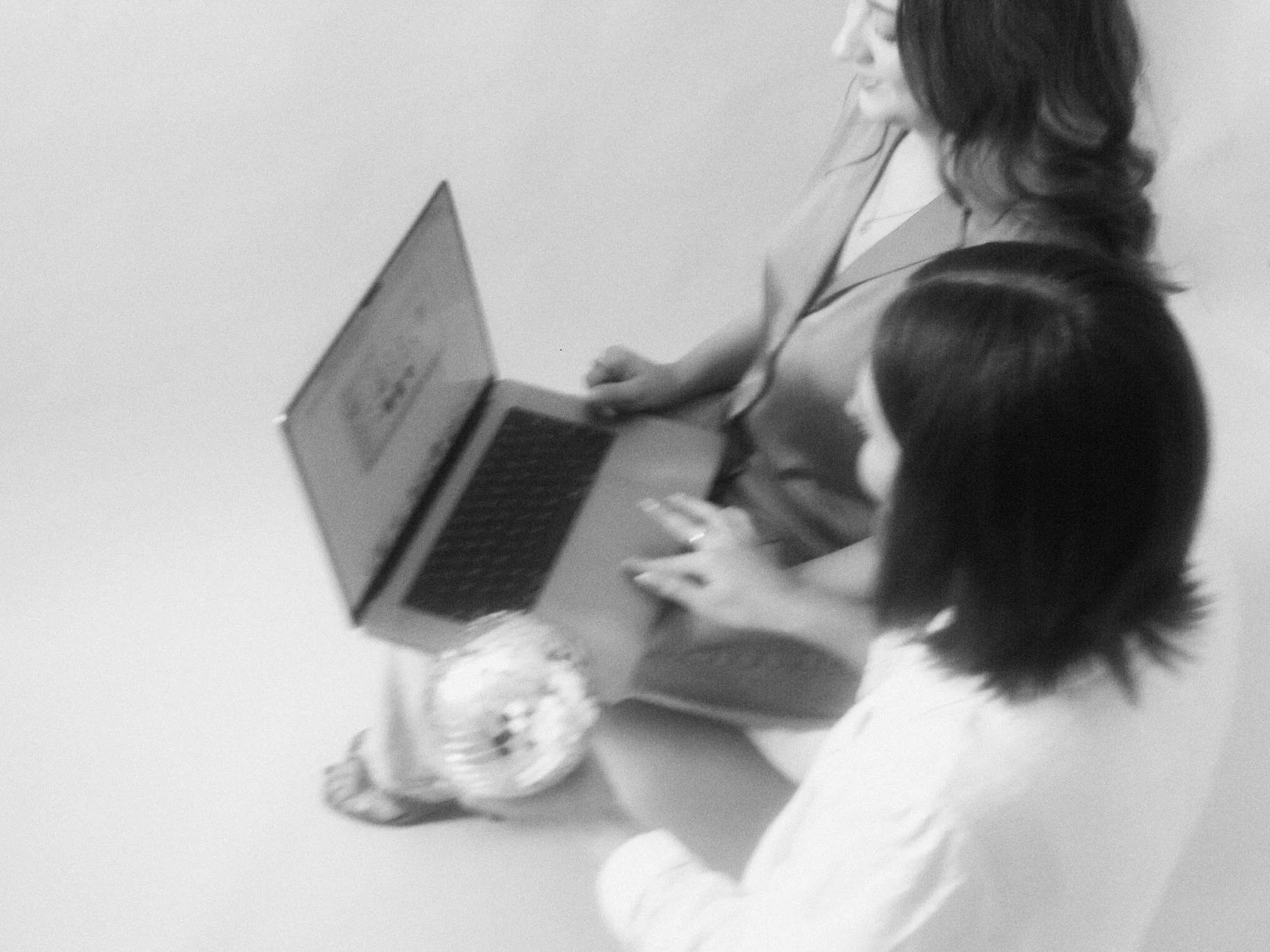 Black and white top down shot of Cass and Amanda, cofounders of Foxtrot Branding working, on a laptop together and holding a disco ball