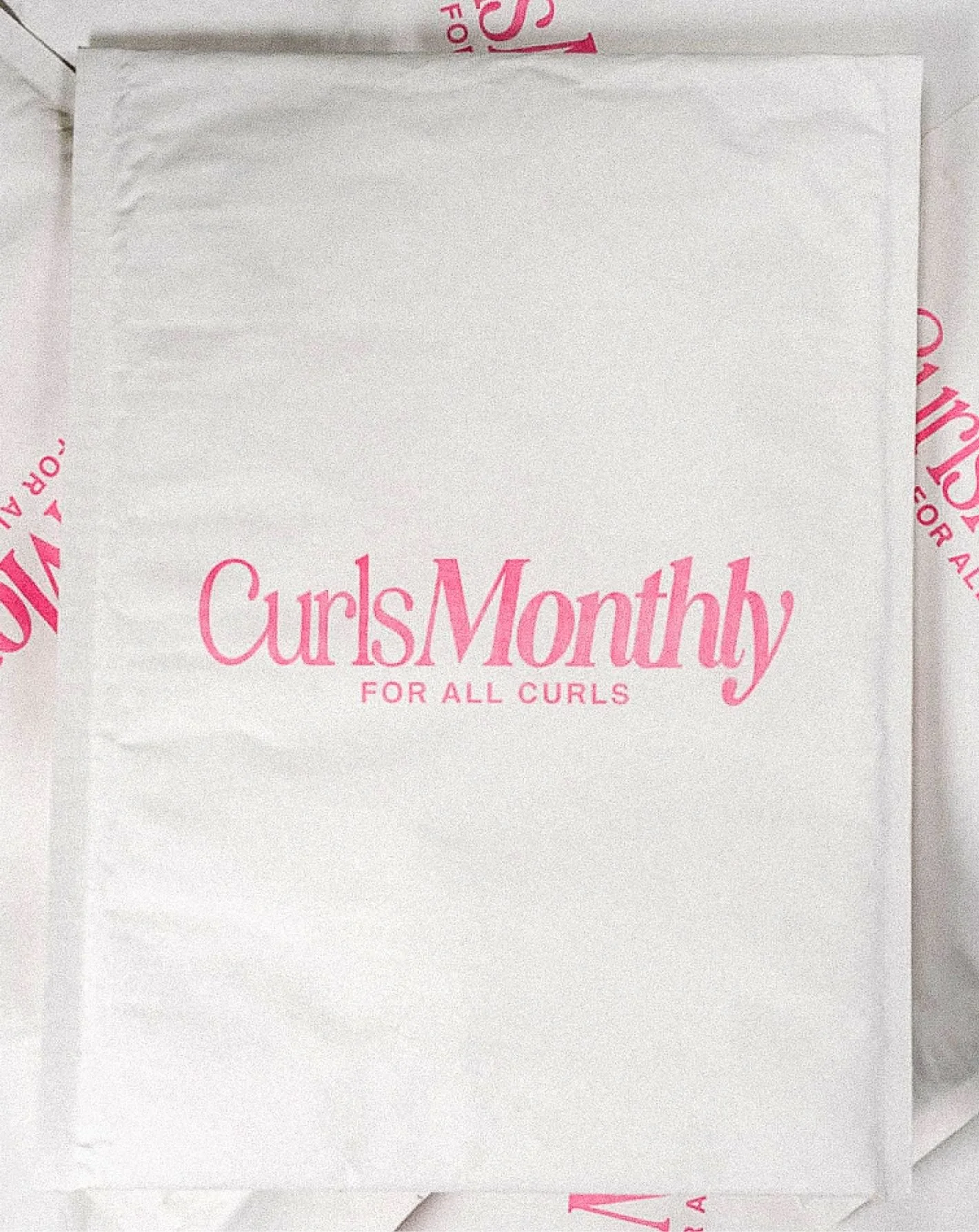 White paper mailer with pink "Curls Monthly For All Curls" Logo on it
