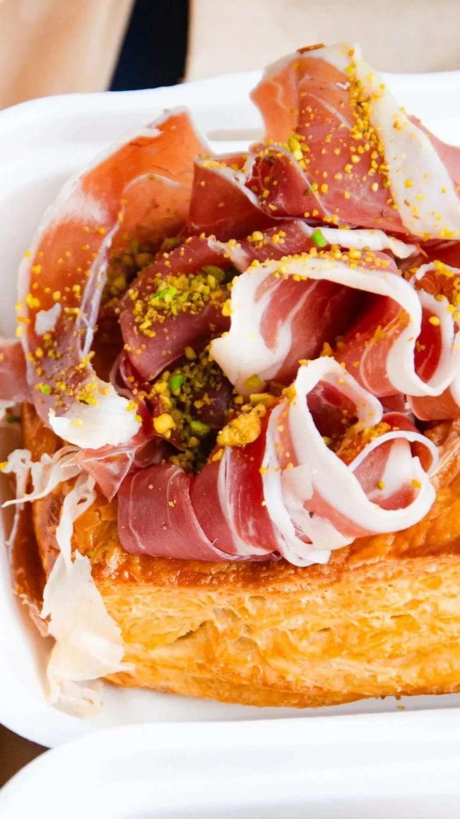 a croissant based pastry with prosciutto and pistachio on top.
