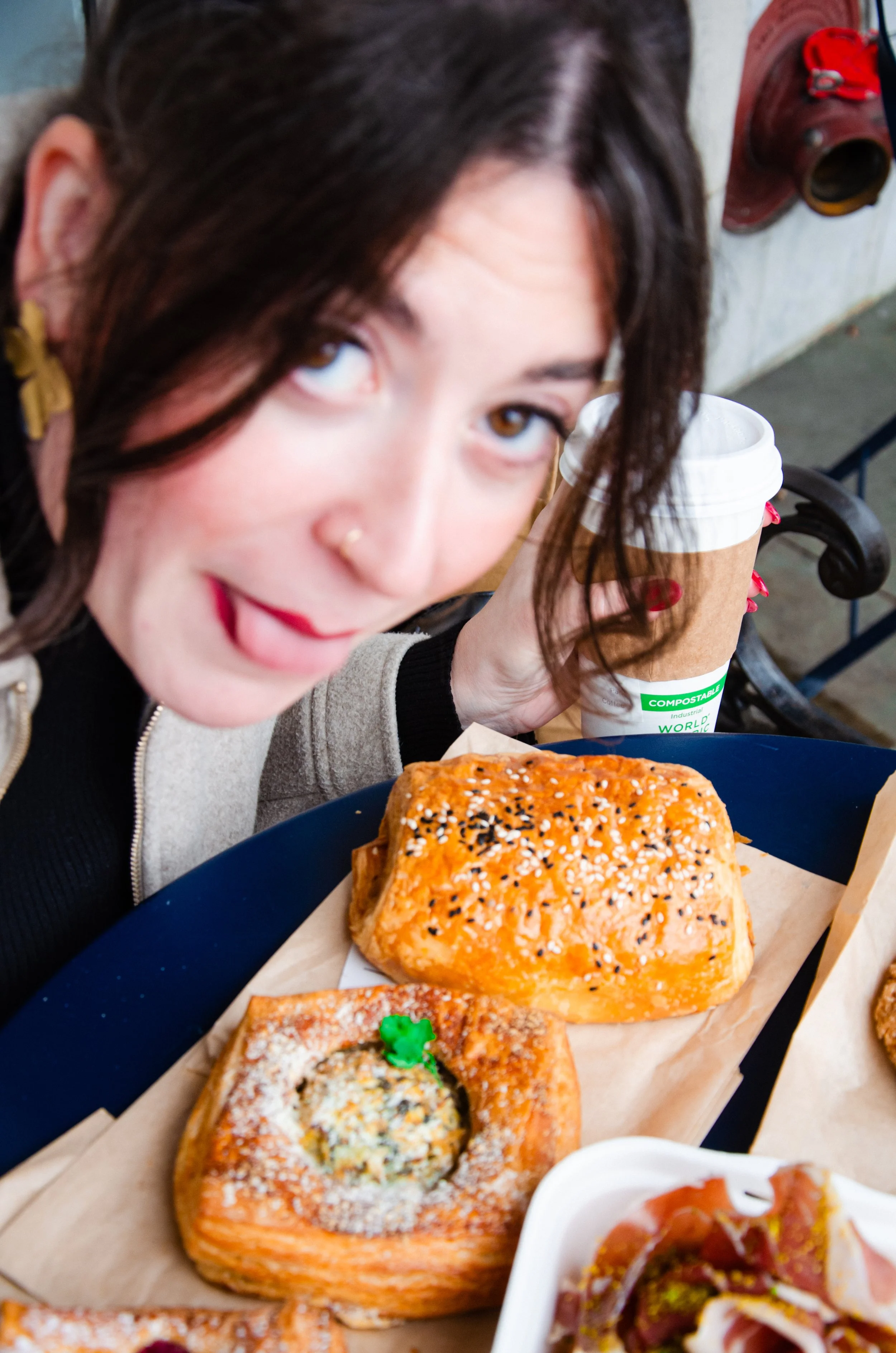 Camille leans in toward the pastries and sticks her tongue out. She is out of focus but the pastries are in focus.