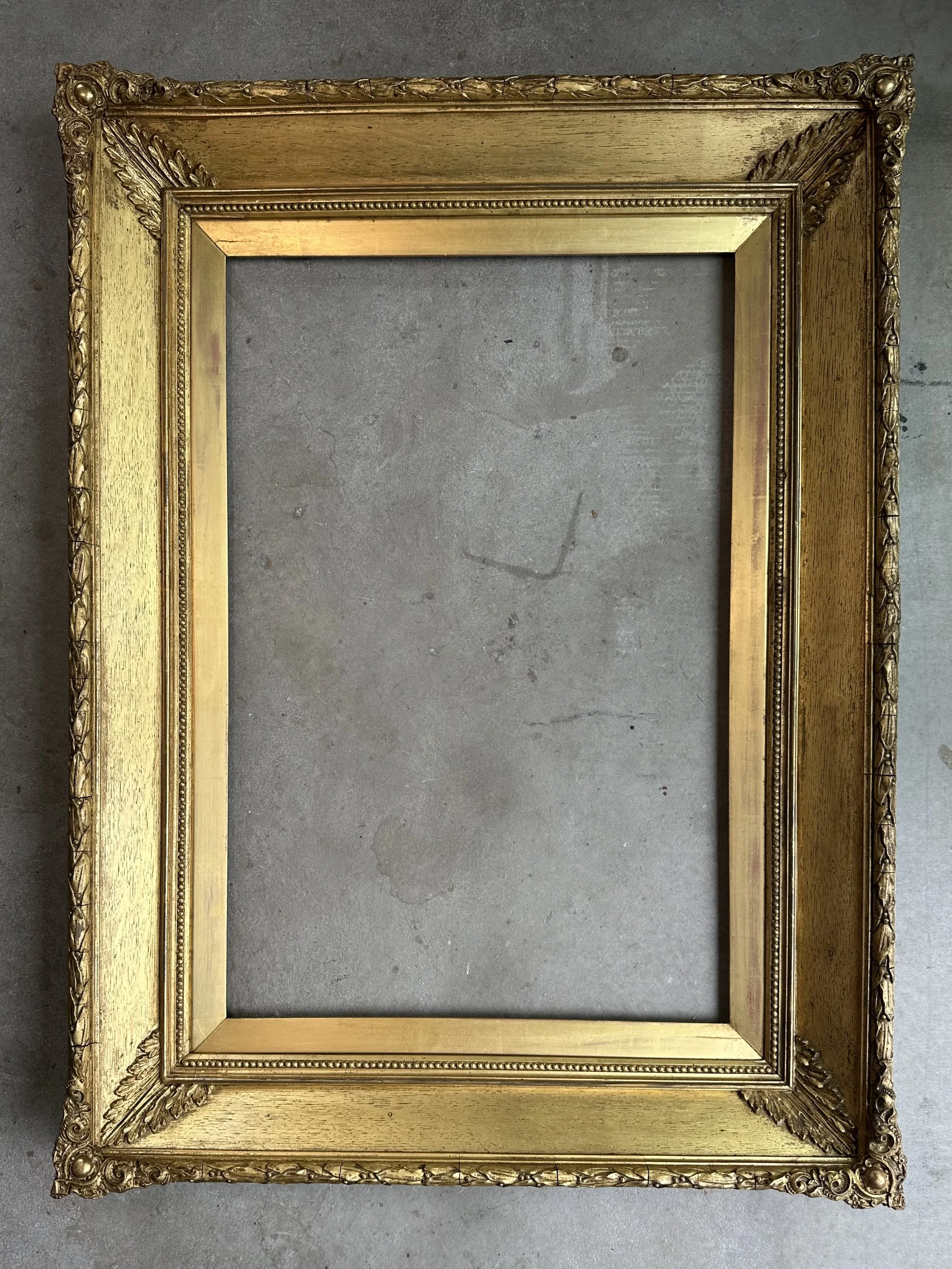 Empty antique gold ornate picture frame on a concrete floor.