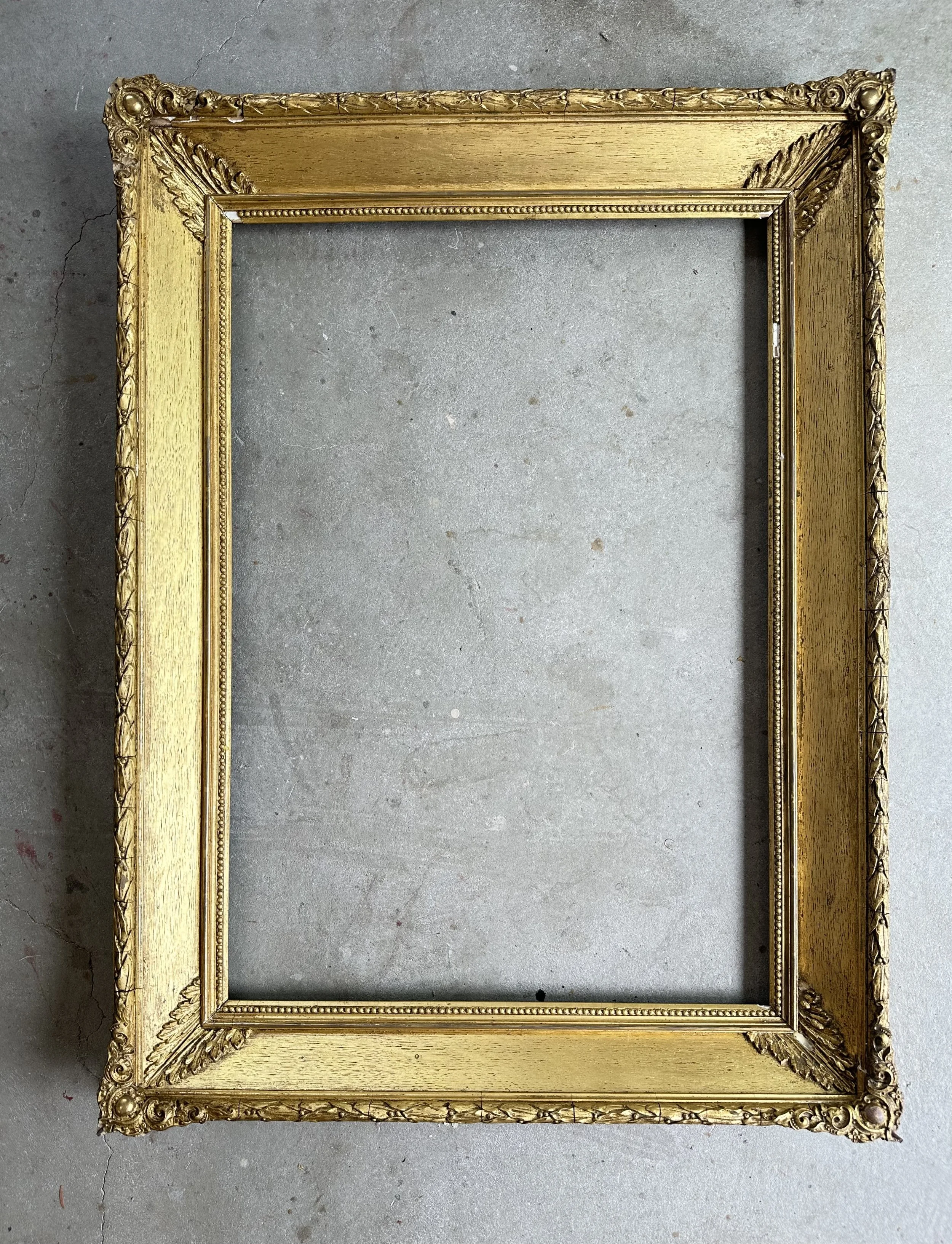 Empty gold ornate picture frame on gray concrete floor.