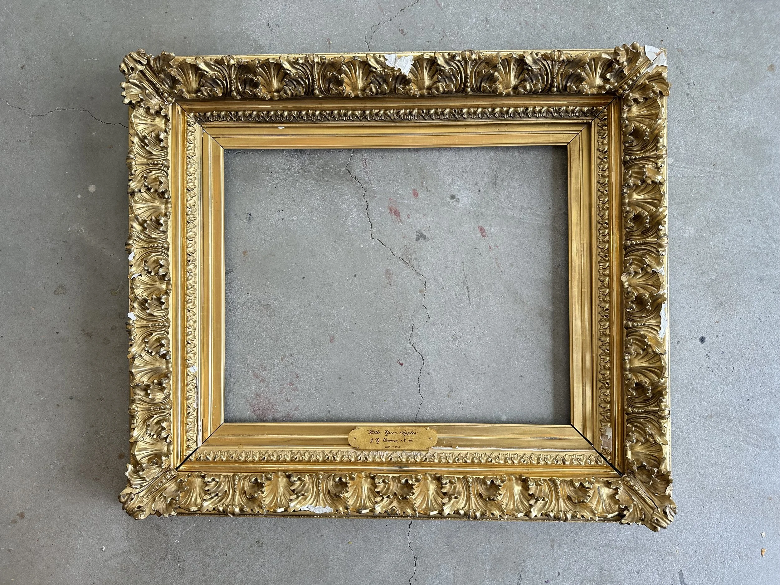 Empty ornate gold picture frame lying on concrete floor.
