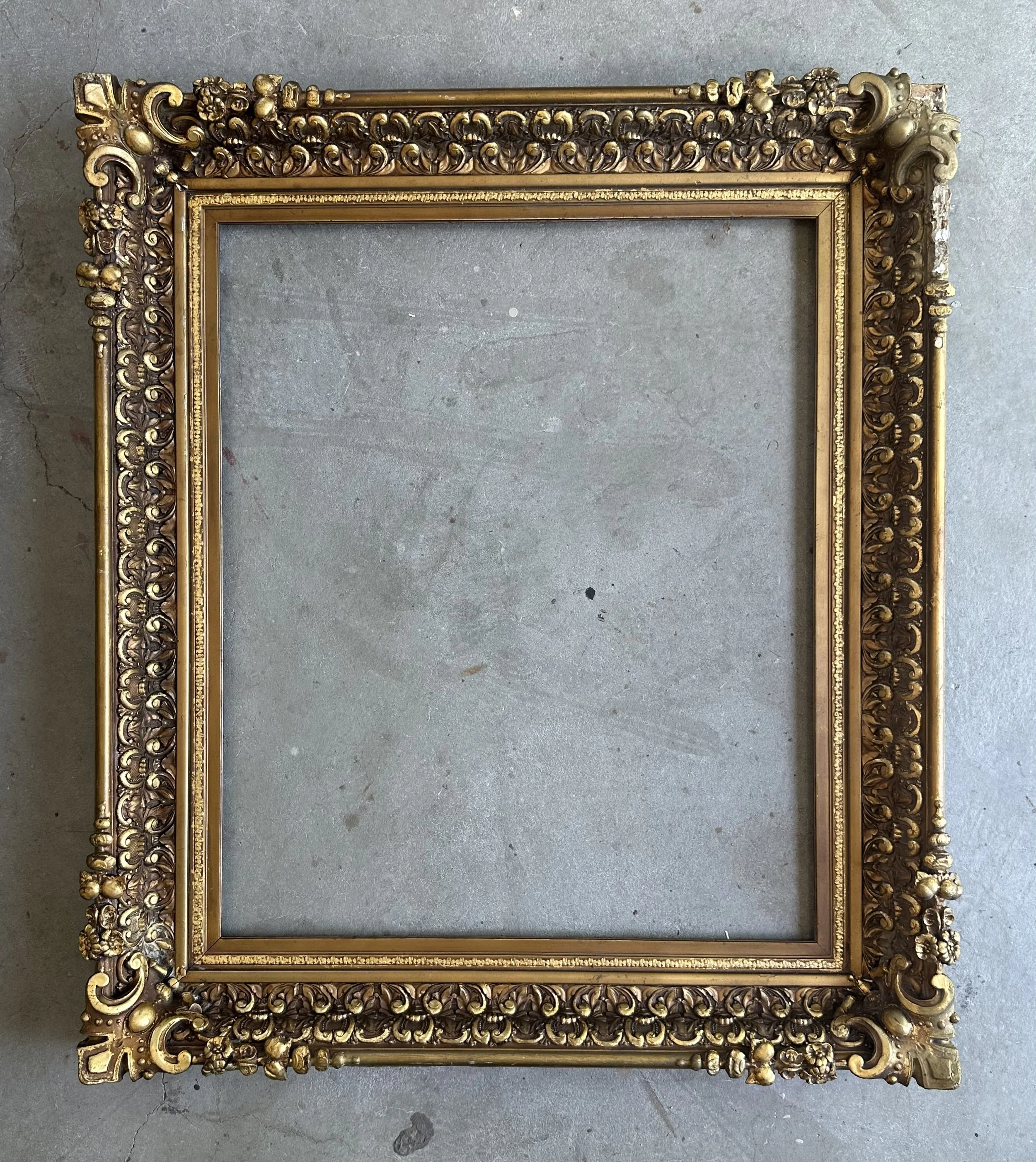 Empty ornate gold and wood picture frame on a concrete floor.